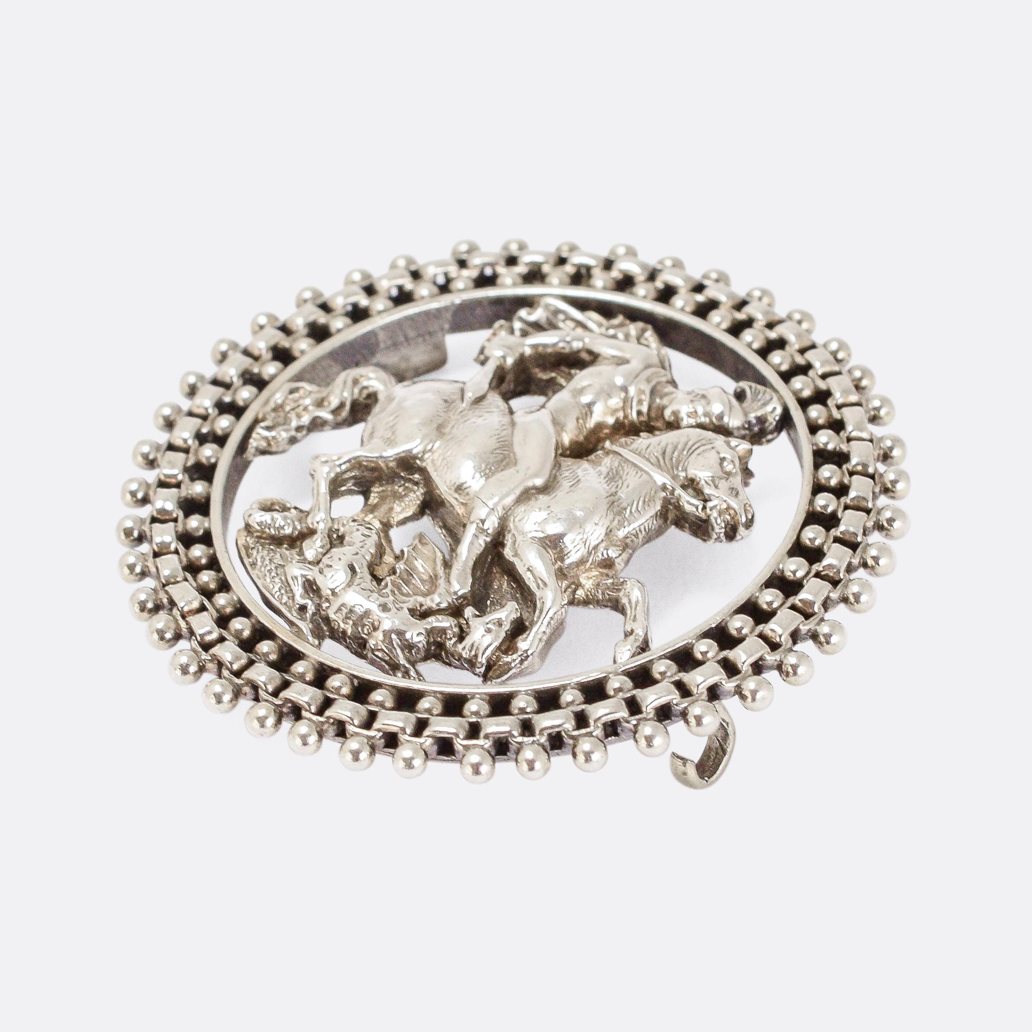 A cool antique brooch depicting the famous scene of St George slaying the Dragon (as featured on gold sovereigns). It's crafted in sterling silver and dates from the latter half of the 19th Century, with a particularly ingenious chain border (which