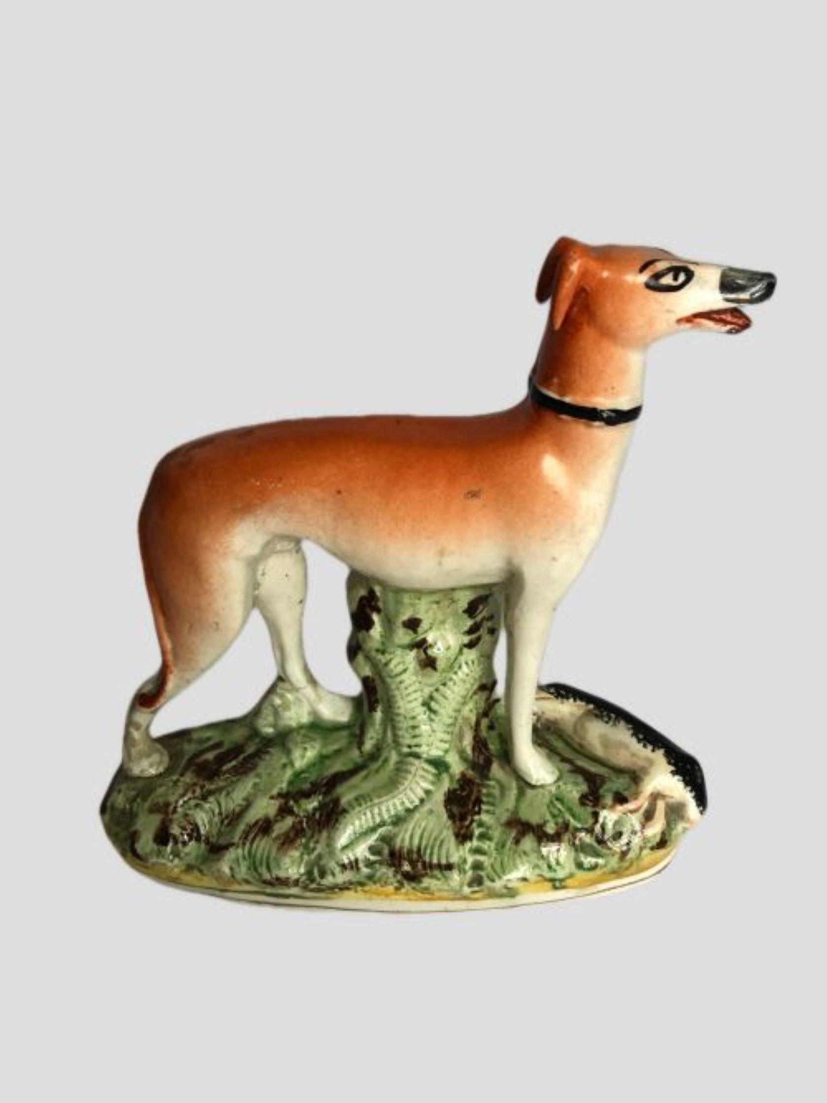 Ancienne figurine victorienne en Staffordshire représentant un chien lévrier. Merveilleuse figurine en brun et blanc d'un lévrier se tenant sur une base ovale avec des feuilles vertes.