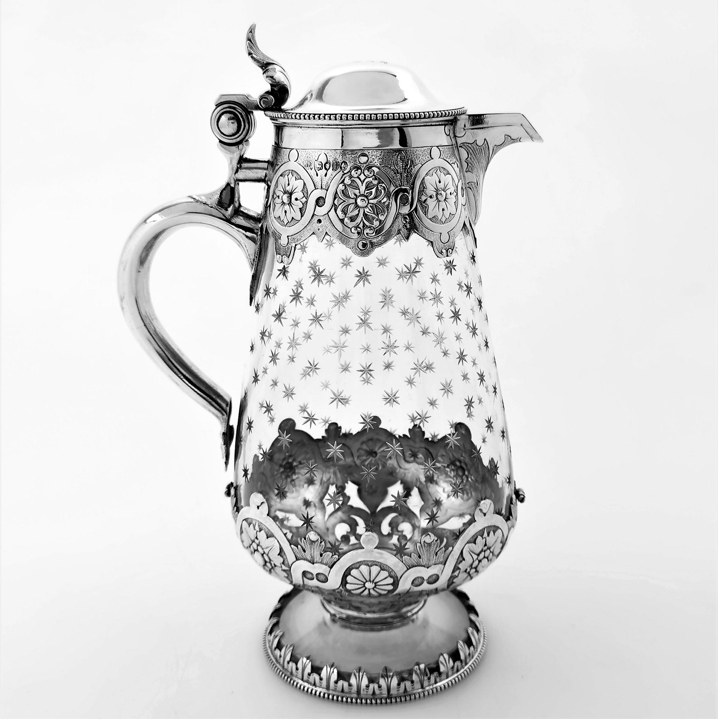 A lovely Antique Victorian solid Silver mounted Claret Jug with a clear glass body. The Claret Jug is decorated with band of ornate chased designs on the upper and lower parts of the body. The Jug has a plain domed hinged lid with a small crest