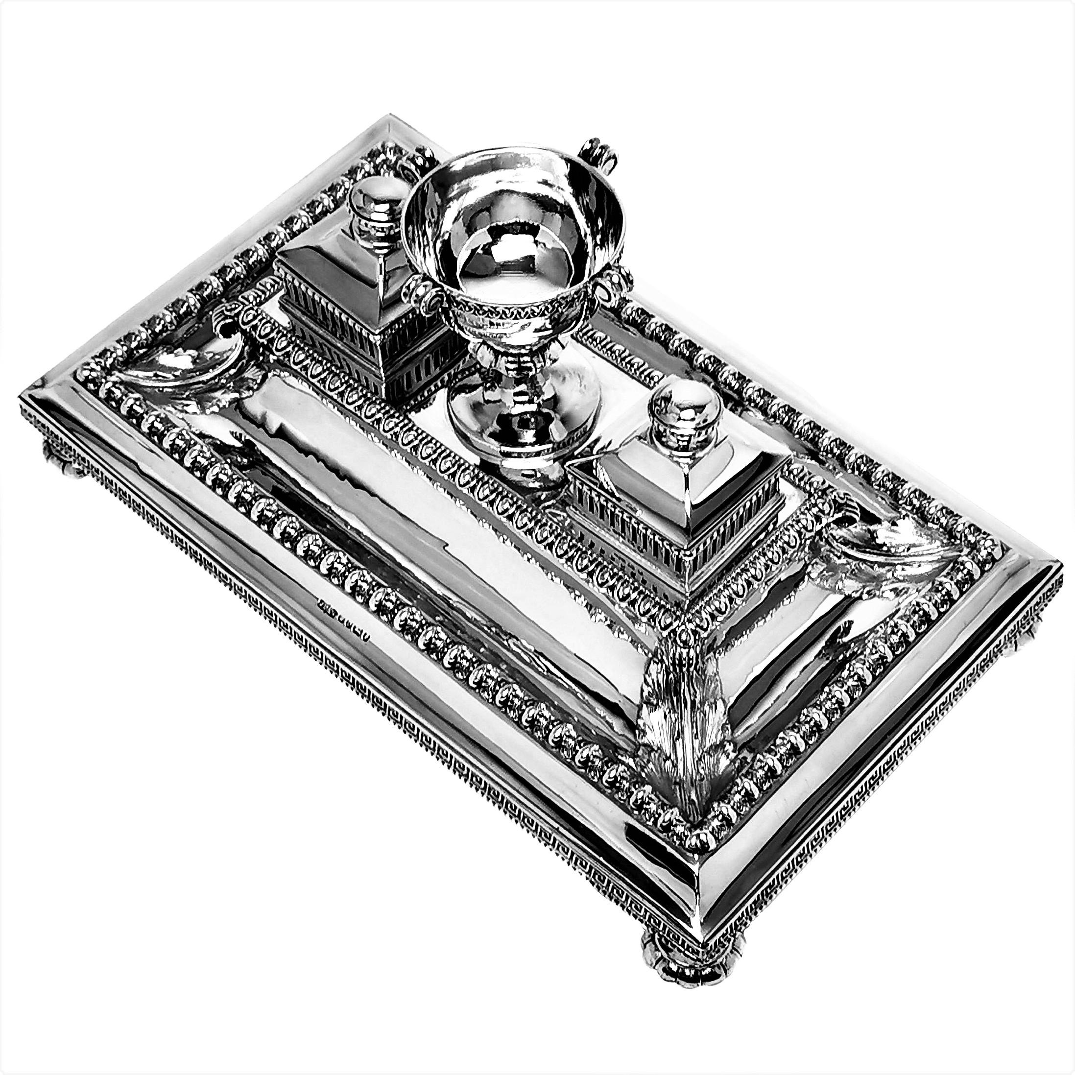A beautiful Antique Victorian Solid Silver Inkstand with two glass lined Inkwells with hinged lids. The base of the inkstand has a classic Greek Key pattern around the sides and rows of chased patterning on the body connected with ornate stylised