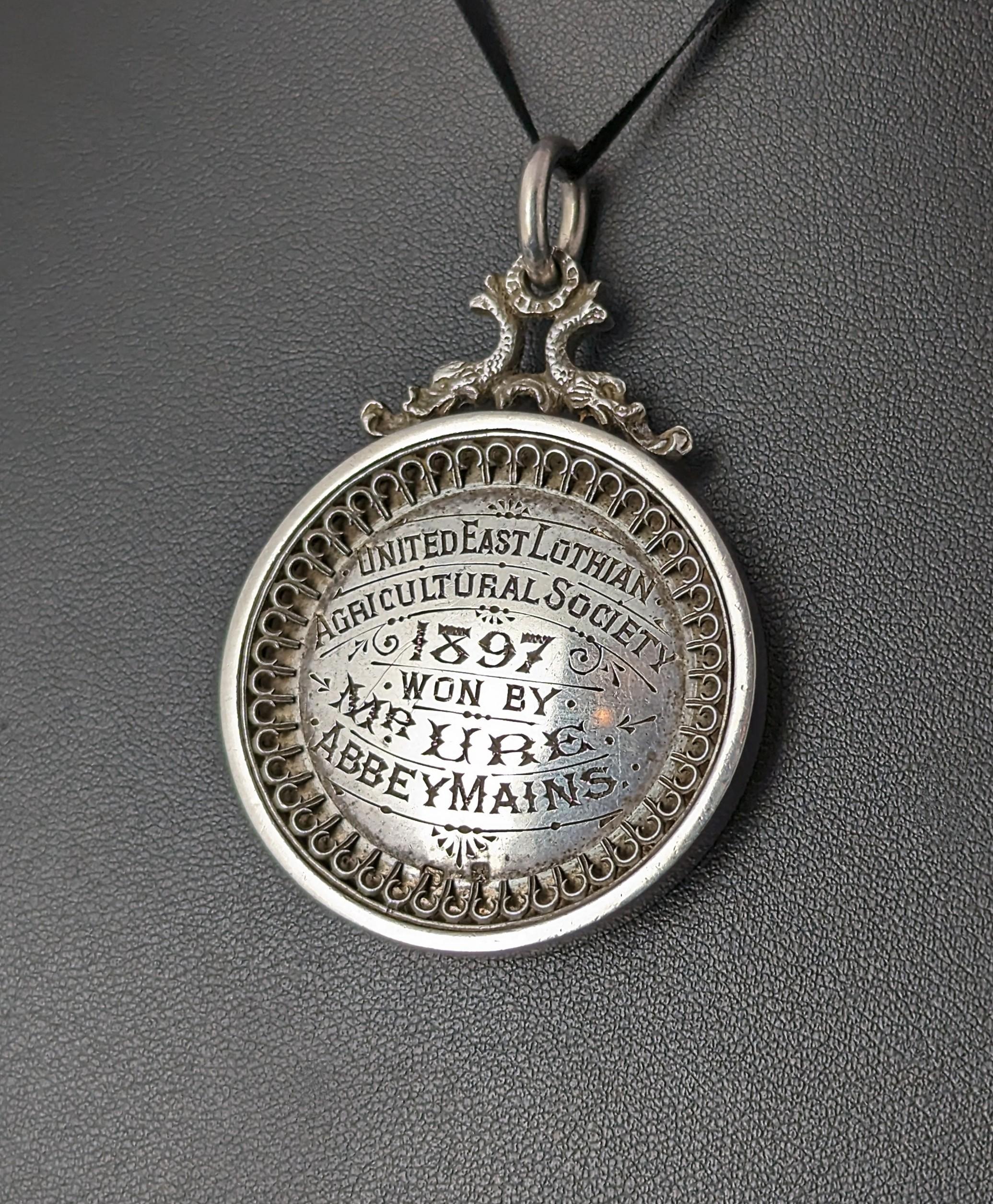 A wonderfully interesting piece here.

I truly love this piece it is so rich in history and Victorian design, there are two medals made from sterling silver, each with a beautifully engraved script to them.

One side reads United East Lothian