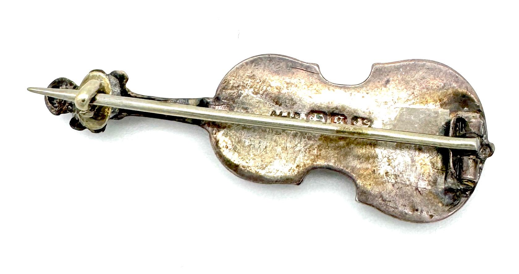 Este novedoso broche victoriano está diseñado en forma de violín. Está hecho de plata de ley. El cuerpo del violín está decorado con flores y hojas grabadas. En el reverso, el pequeño violín hueco lleva una marca de fabricante no identificada