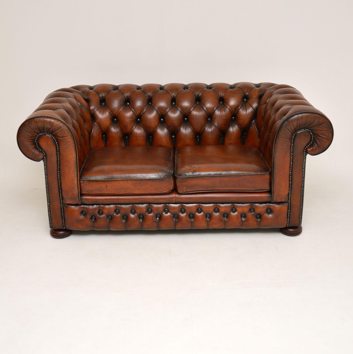 Antique Victorian style 2-seat leather Chesterfield sofa in good original condition and dating to circa 1960s period.

It has a deep buttoned back and arms which roll over the sides and back. There are two loose cushions and it sits on flat bun