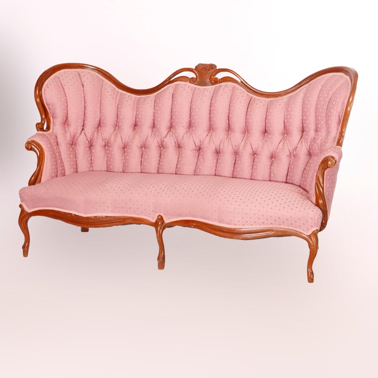 An antique Victorian style sofa offers walnut frame in camel back form with crest having carved fleur de lis flower basket with flanking scroll form elements over tufted back with scroll form arms, raised on cabriole legs, c1920

Measures - 41.5''