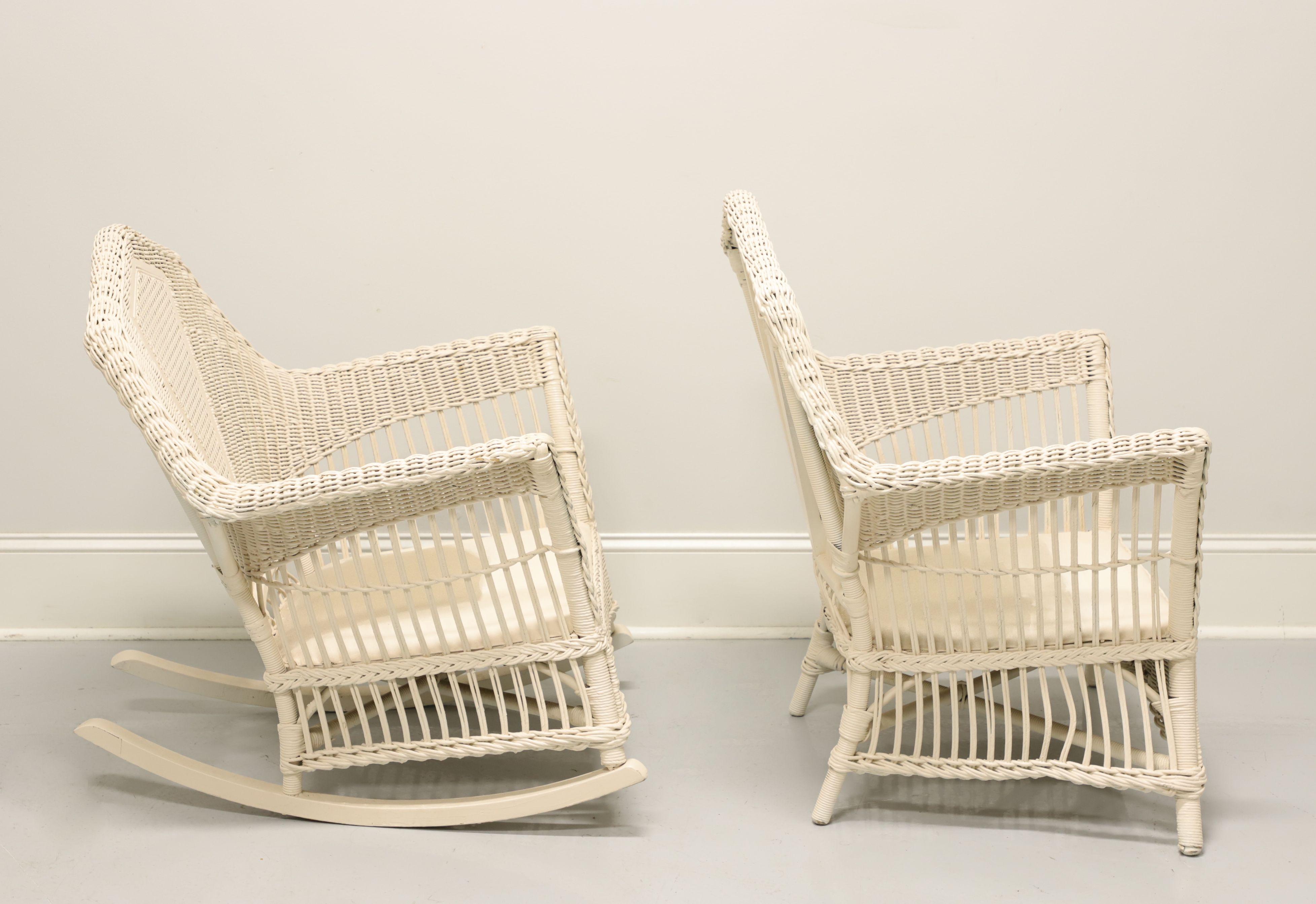 An antique Victorian wicker armchair and rocking chair pair, unbranded, in the manner of Heywood-Wakefield. White painted woven & stick wicker reed, cane, wood frame, canvas and metal spring cushion support. Features wicker wrapped frame, ornately