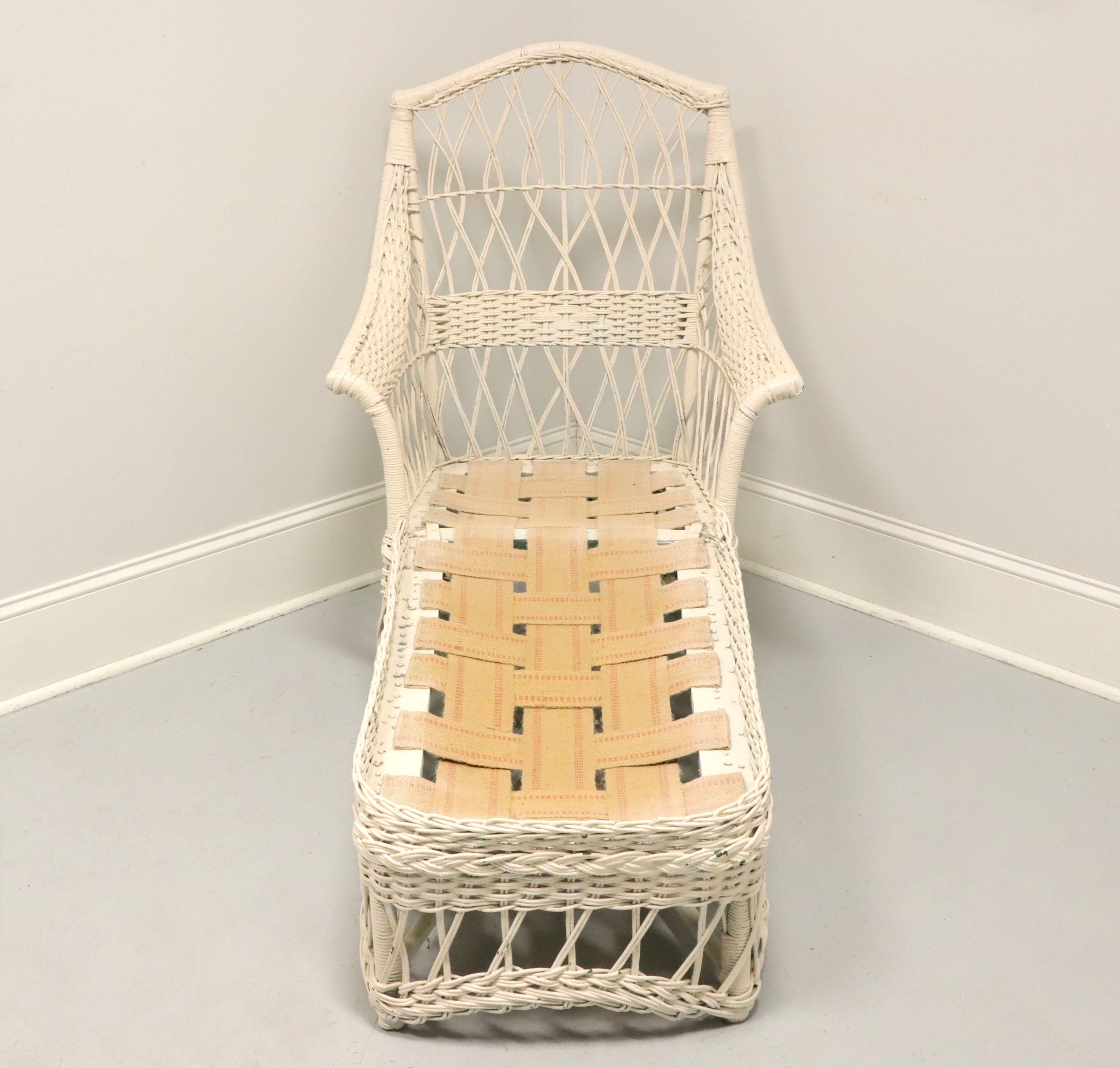 An antique Victorian wicker chaise lounge, unbranded, in the manner of Heywood-Wakefield. White painted woven & stick wicker reed, wood frame and webbed jute strap cushion support. Features wicker wrapped frame, ornately woven & stick diamond design