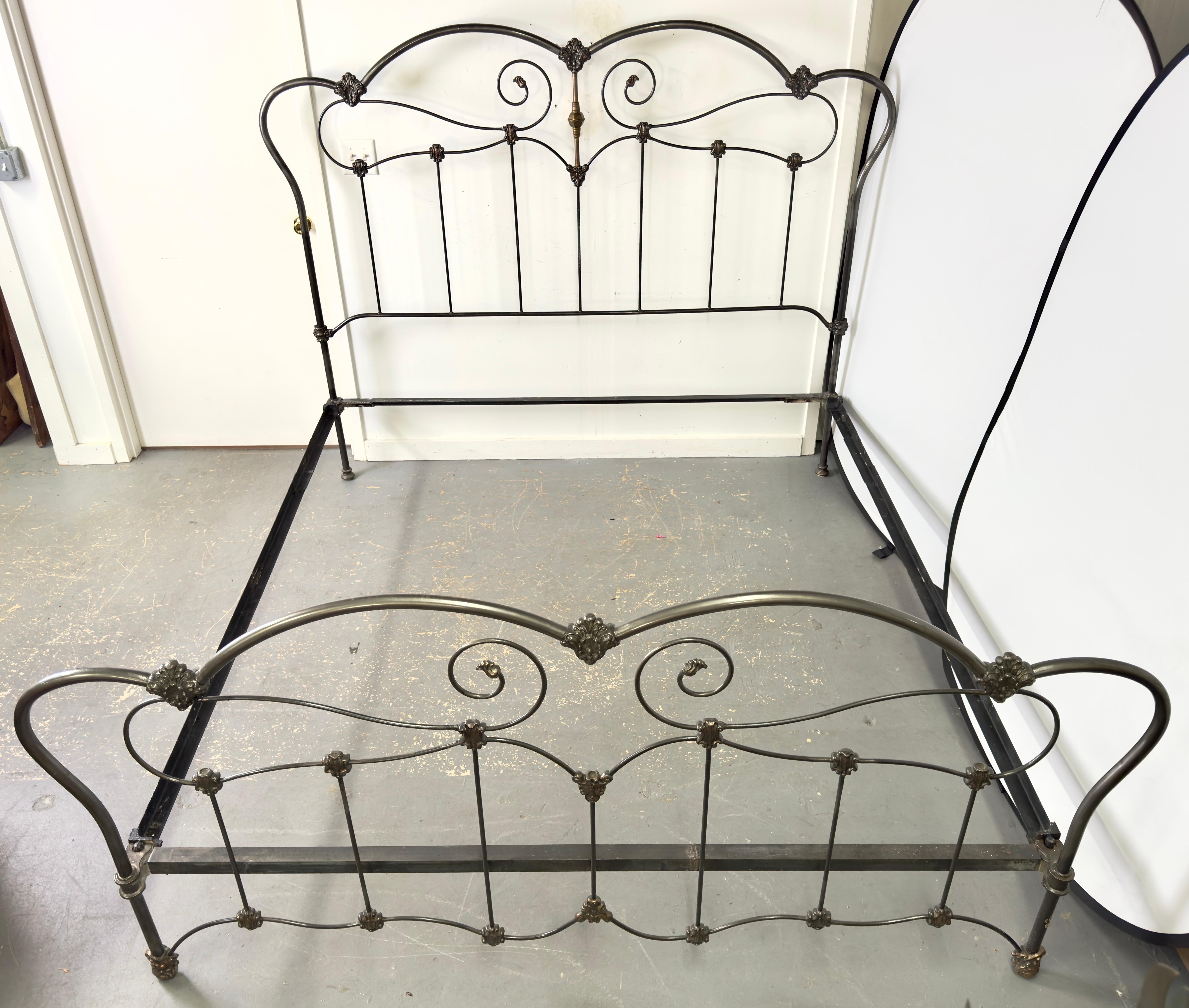 A  19th Century Victorian style wrought iron king bed frame. The headboard and footboard are adorned with gracefully curving scrollwork, meticulously forged to create a harmonious blend of strength and delicacy. Each curve and twist in the ironwork