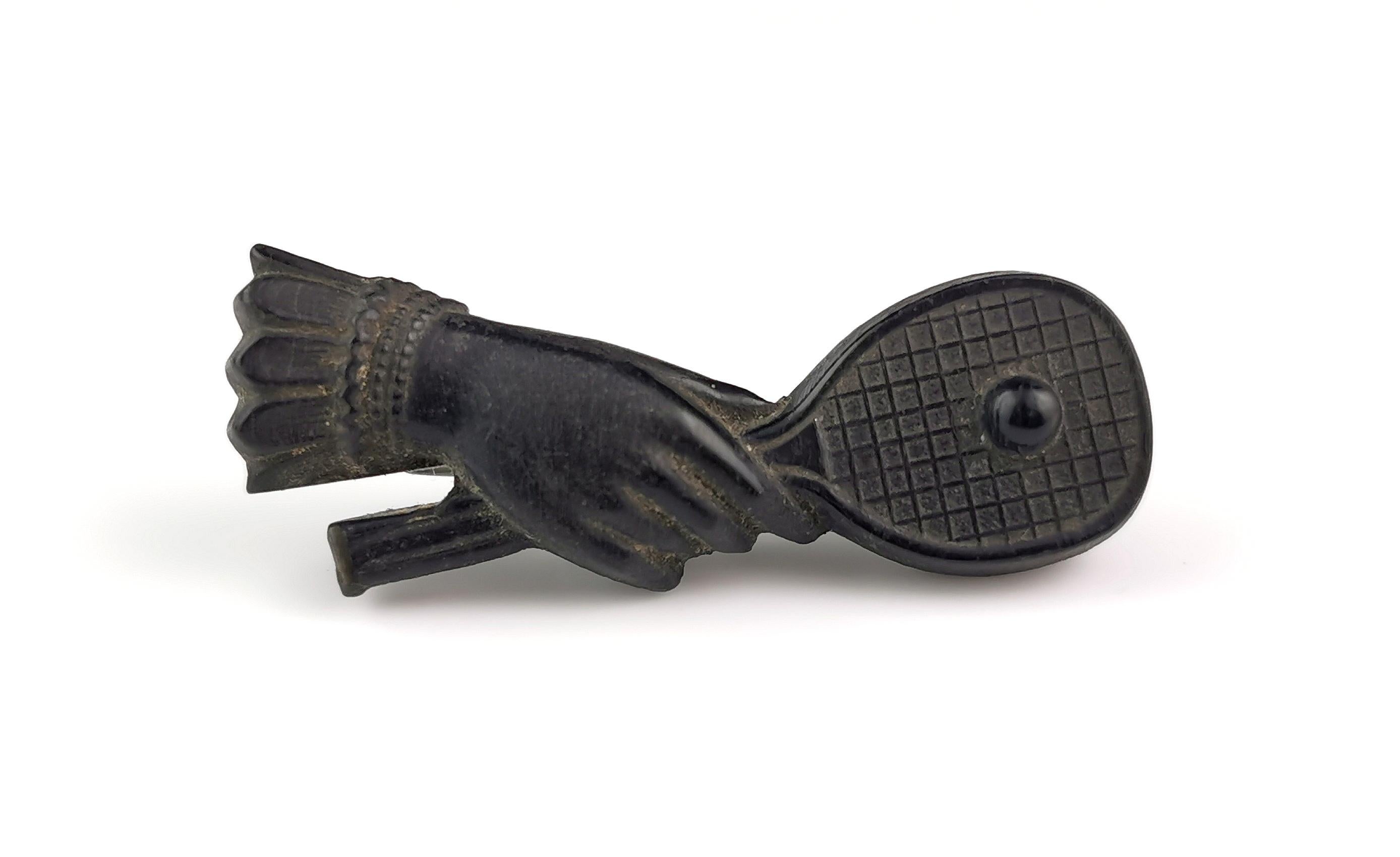 An interesting and well detailed antique Victorian tennis brooch.

It features a cuffed hand holding a tennis racket with a ball.

The brooch is made from bog oak and further lacquered black.

It is has an old c type clasp and pin fastener this is