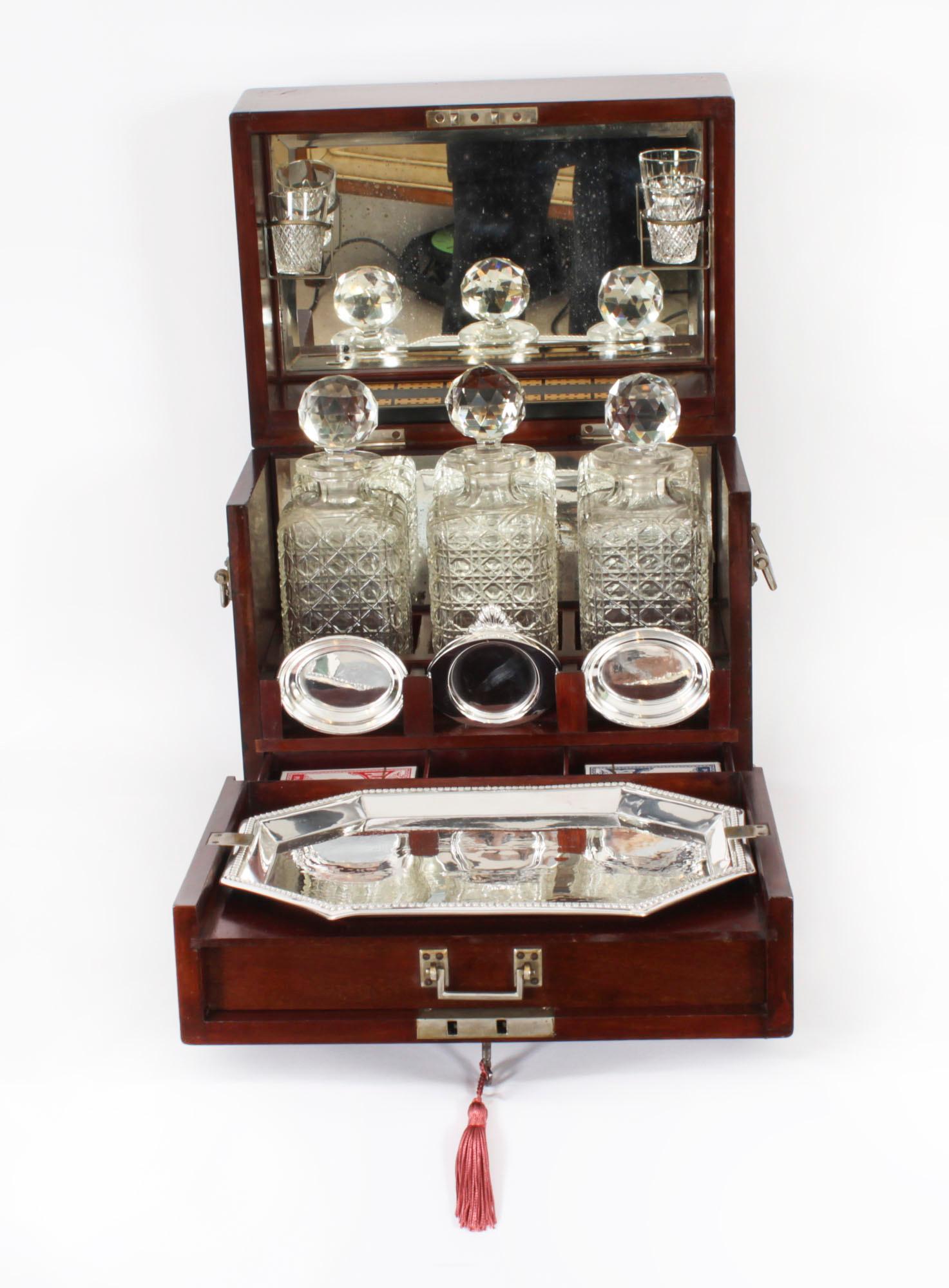 This is a fabulous antique Victorian games compendium and  tantalus, circa 1880 in date.

It consists of three cut crystal liquor bottles with stoppers, a pair of engraved shot glasses, a silver plated tray and a fitted cribbage board, all housed in
