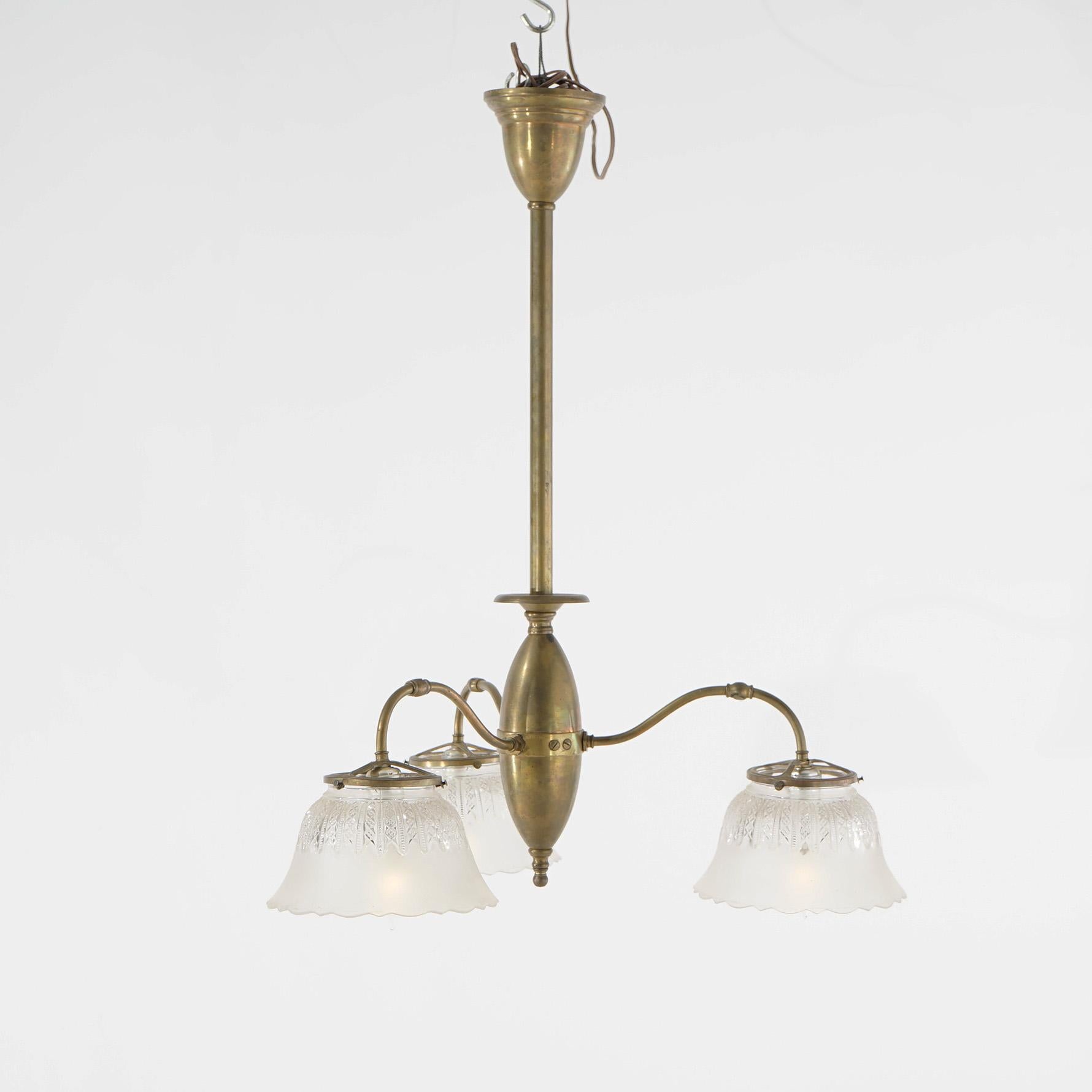 An antique Victorian early electric chandelier offers brass construction with stylized elongated egg form font having three scroll form arms terminating in drop lights with etched glass shades, 19th century

Measures- 30.5''H x 24''W x 24''D