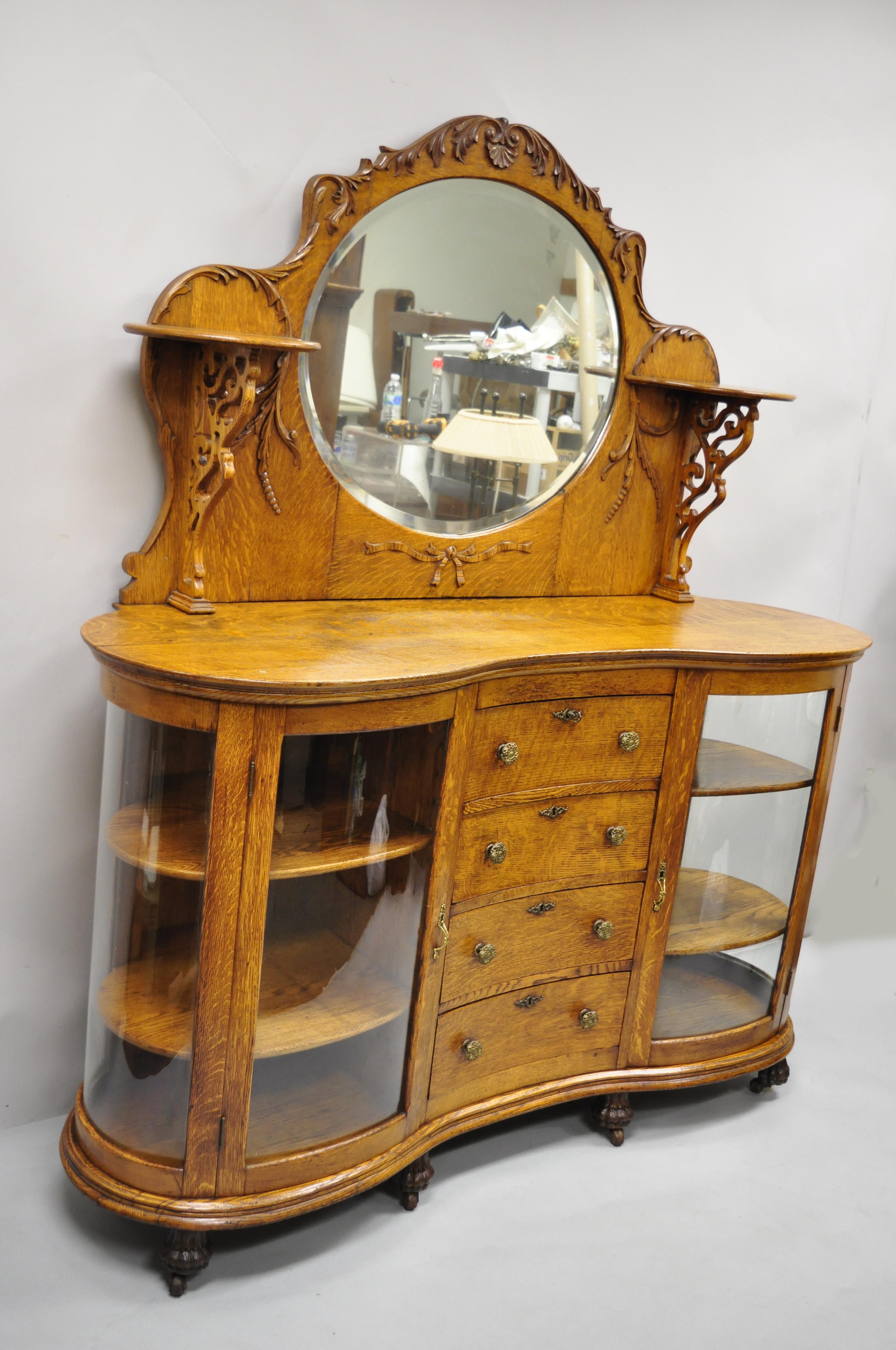 Antique Victorian tiger oak carved paw feet sideboard buffet with bow curved glass china cabinet base. Item features (4) curved glass panels, serpentine front, beveled glass mirror backsplash, 2 upper shelves, curved paw feet on casters, solid wood
