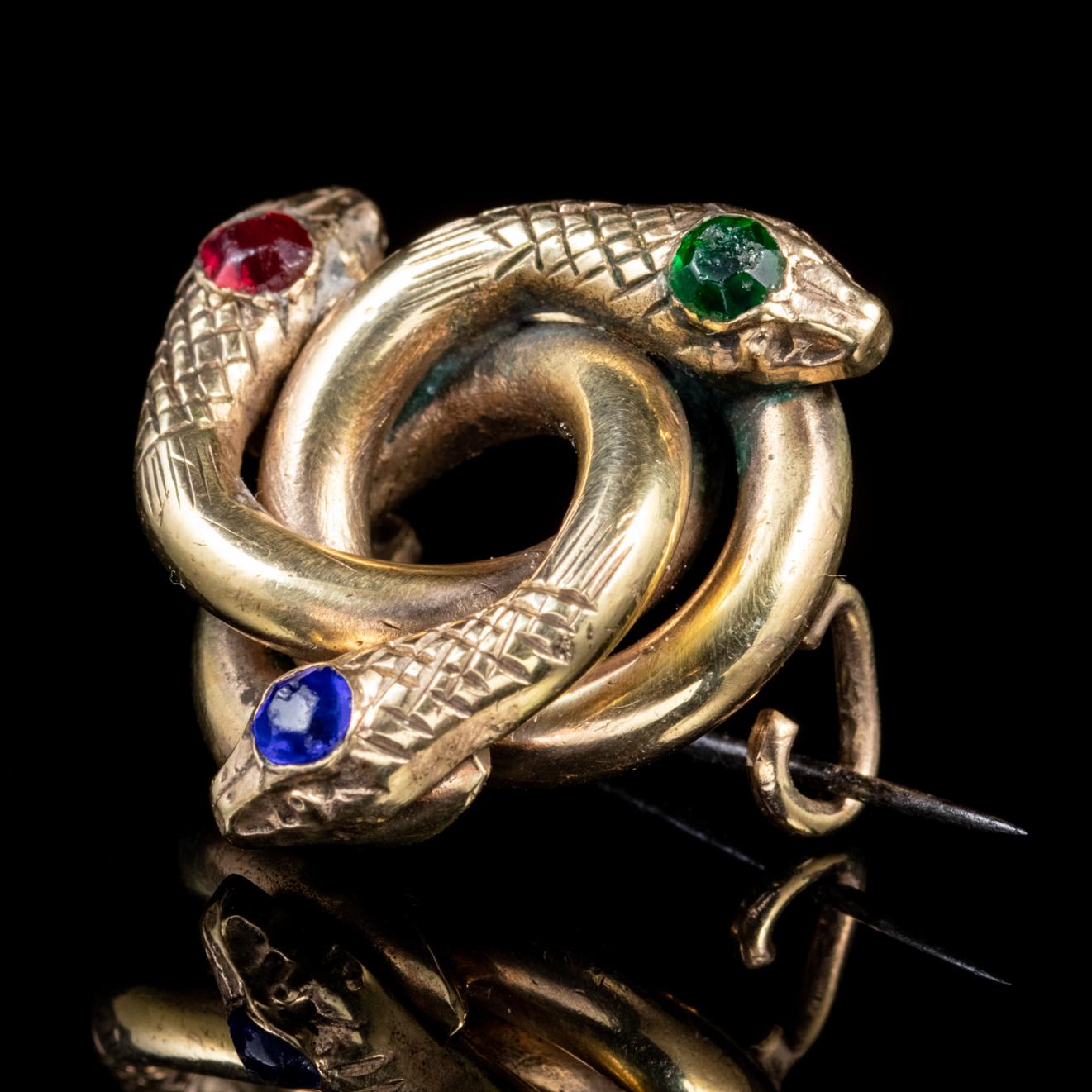 This fabulous Victorian snake brooch is set in Steel, gilded in 18ct Yellow Gold and depicts three coiled serpents, each crowned with a Paste stone in blue, red and green.

Serpent jewellery became popular in the Victorian era and symbolized a