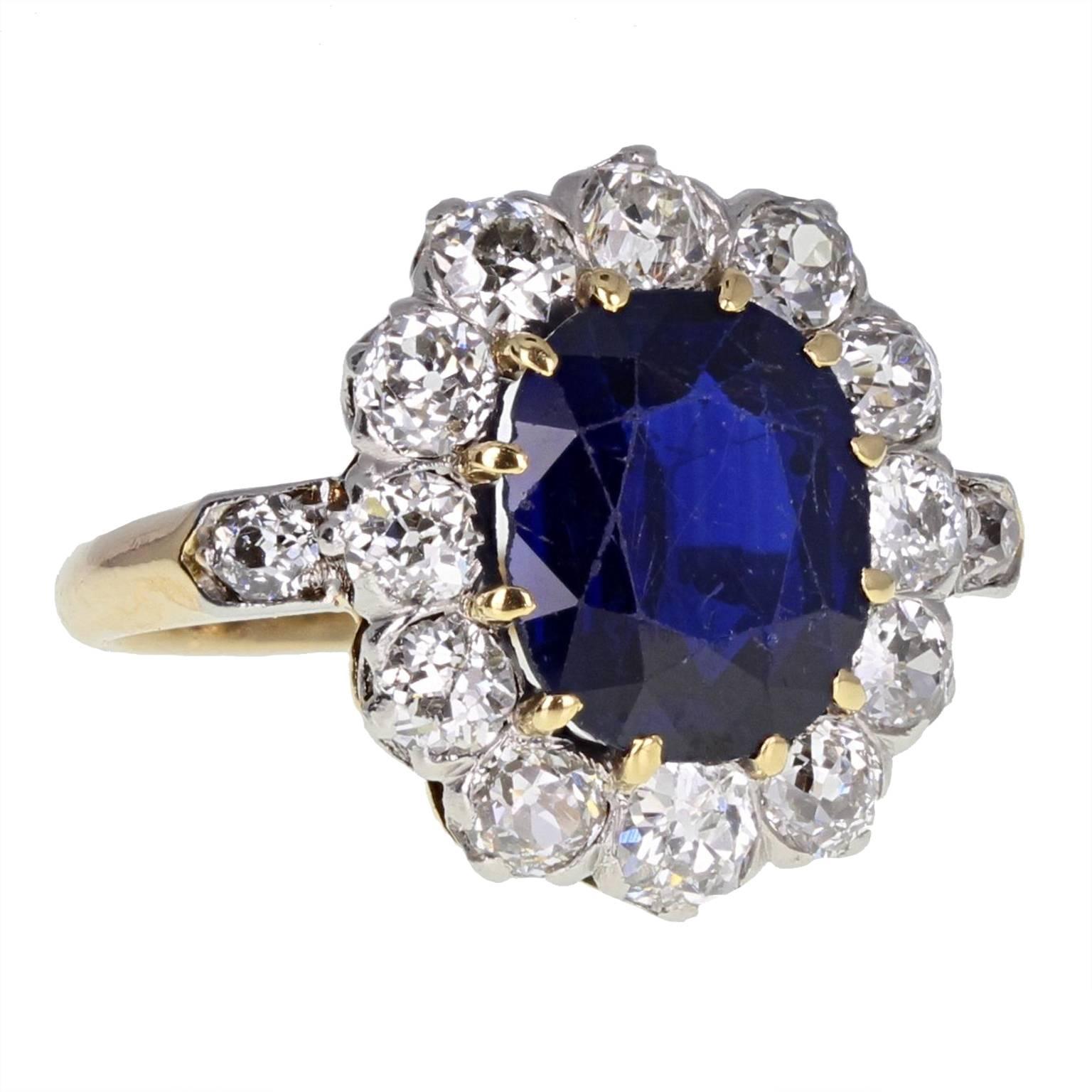 An exquisite Victorian sapphire and diamond cluster ring from circa 1900. The central oval-shaped blue sapphire mounted in 18-carat gold claws, surrounded by 12 old-cut diamonds. A single old-cut diamond set in each shoulder. Polished 18-carat