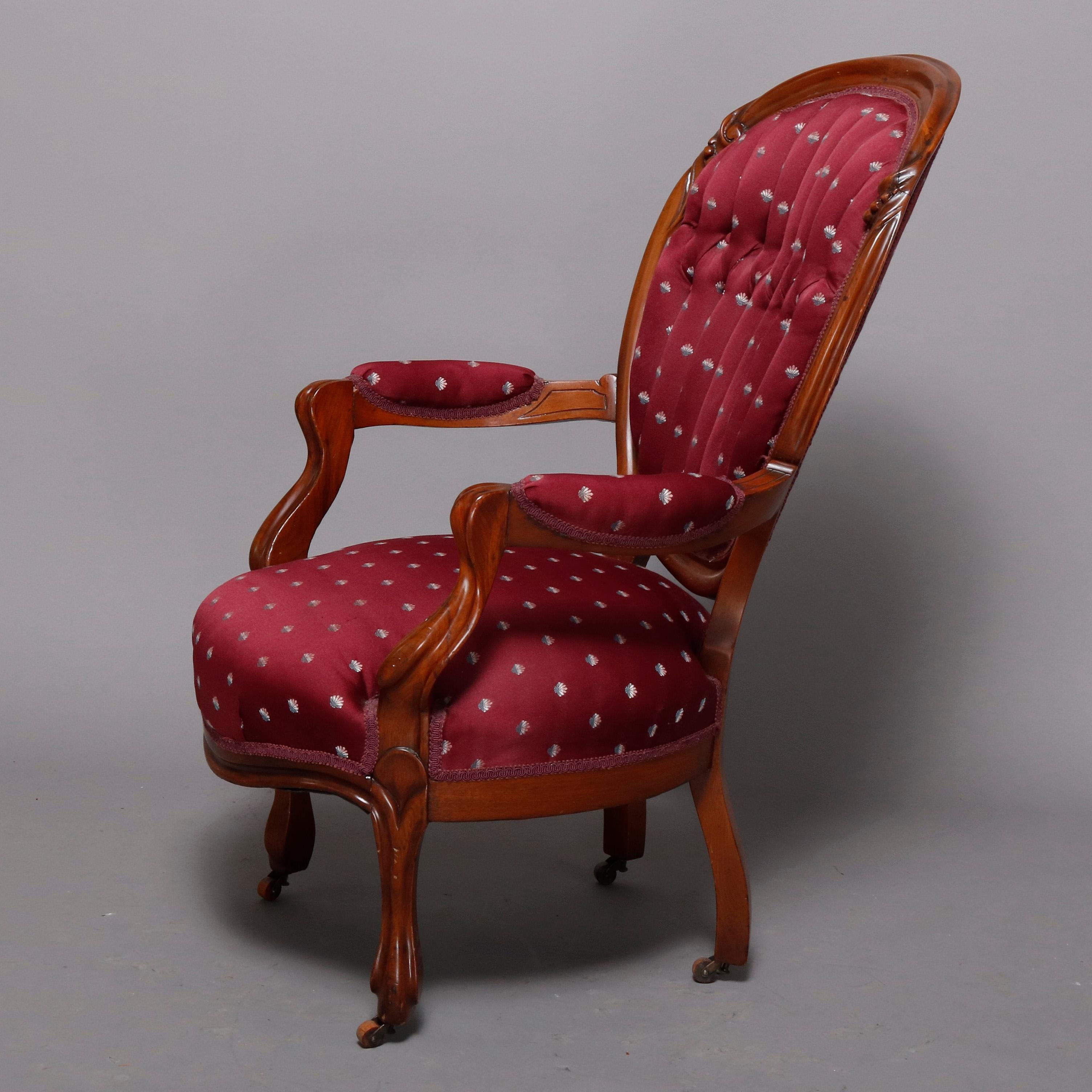 An antique Victorian parlor armchair features finger carved walnut frame with medallion back having button back upholstery, covered arms and seat, raised on cabriole legs terminating in casters, circa 1880

Measures: 40