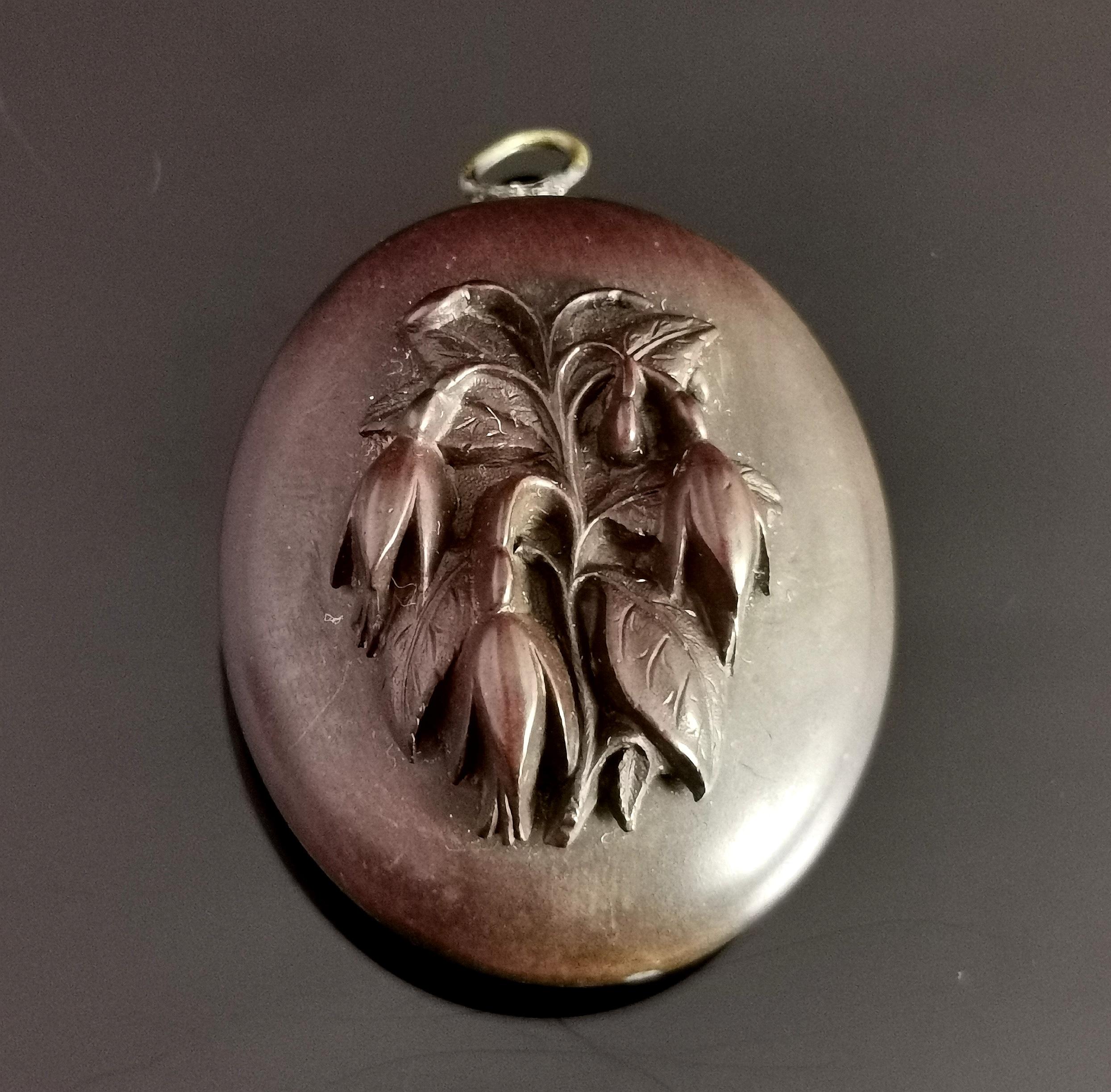 A beautiful antique Victorian mourning locket.

It is a chunky locket made from vulcanite with an applied spray of flowers possibly Fuschia to the front.

The locket has browned with age as is very common with old Vulcanite but it would have been