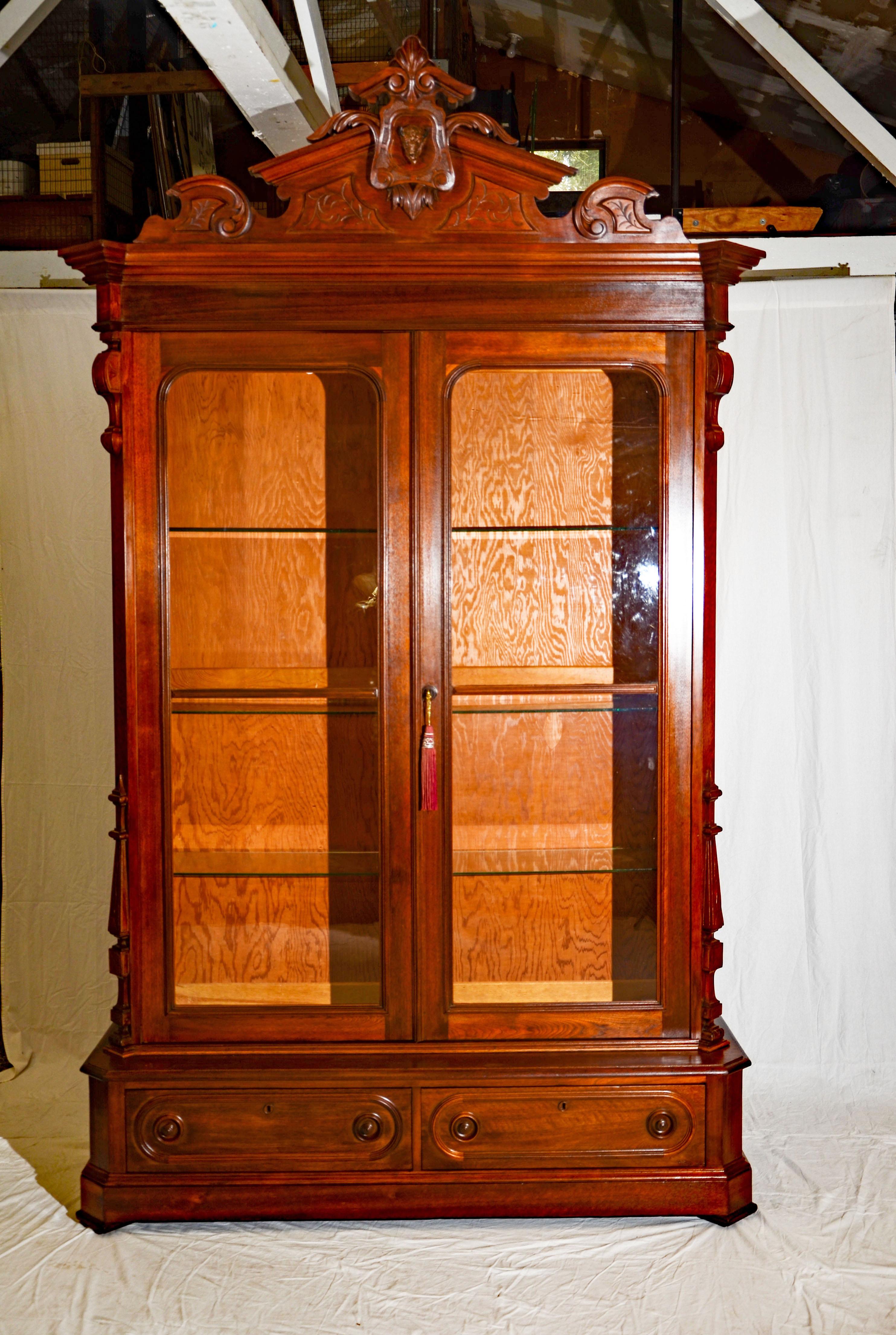 This beautiful American Victorian bookcase or display cabinet disassembles for shipping, there are bolts and screws for re-assembly of a base, to sides, one top, one back, two doors, one crest, and four glass shelves. The base is 20
