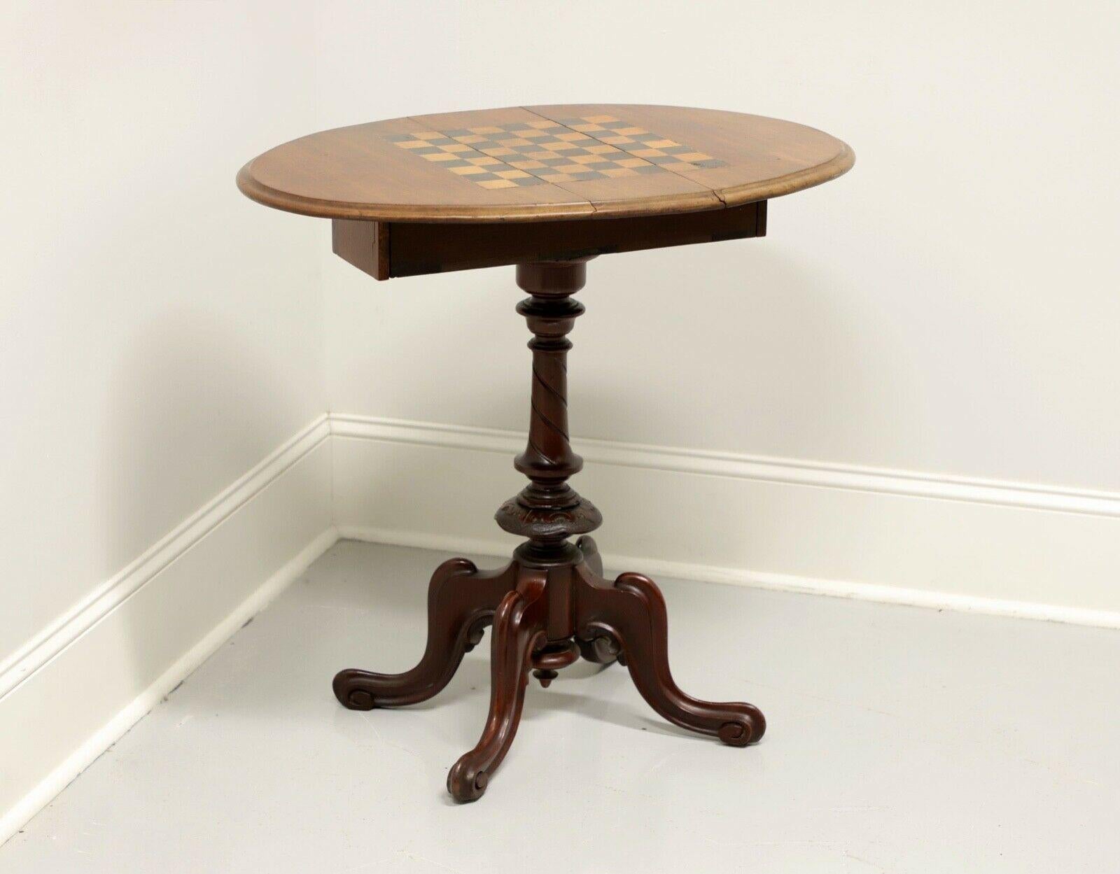 An antique Victorian drop leaf game table, unbranded. Walnut with inlaid game board to top and turned pedestal base with four curved legs. Features drop leaf top that folds up and swivels to form oval games surface. Two drawers provide storage for