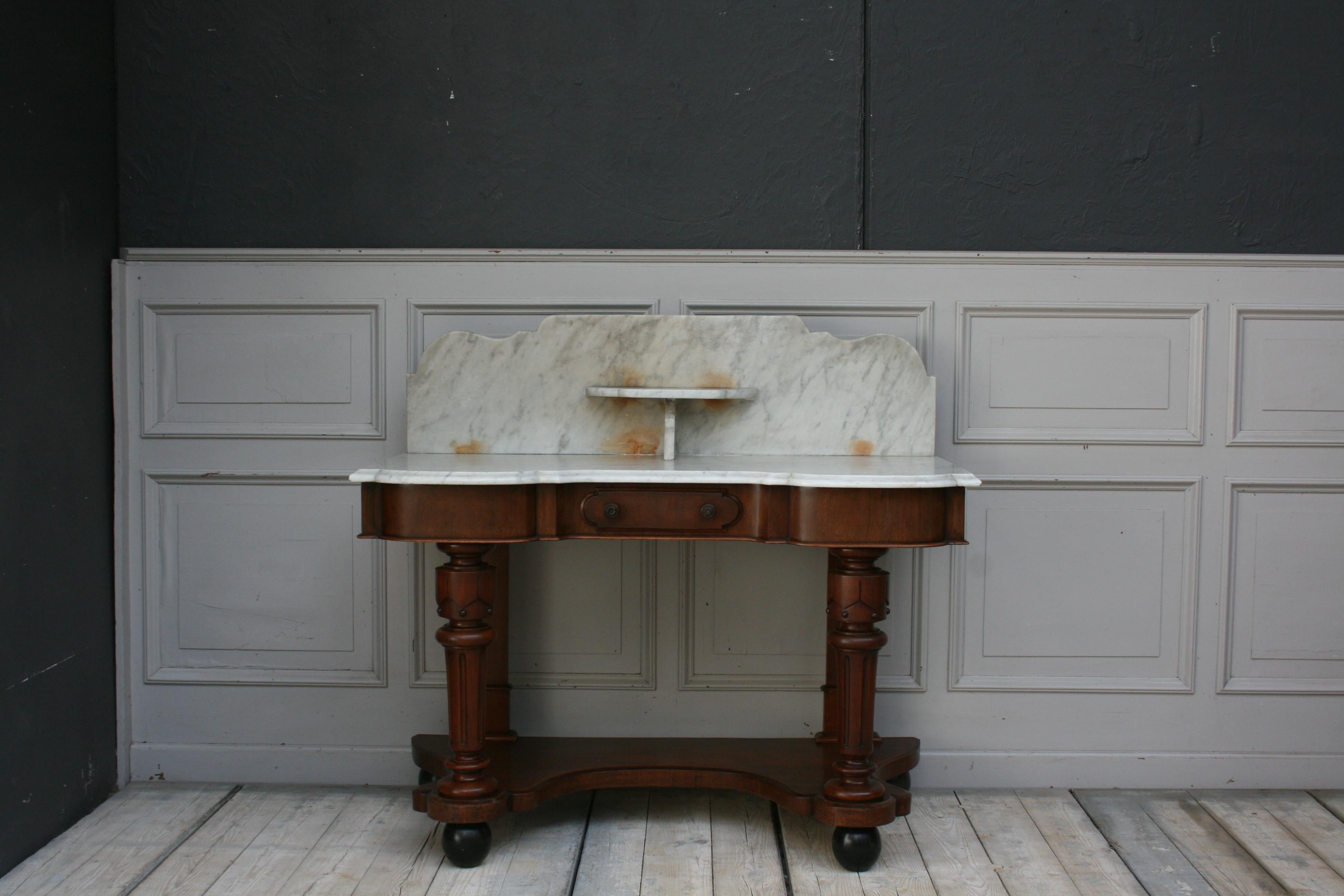 Antique English Victorian washstand, with a marble top with splash and bracket shelf. The mahogany frame with single drawer stands on four decoratively turned and fluted legs with 4, but newly mounted black ball feet. 

Dimensions: 
79/ 110 cm