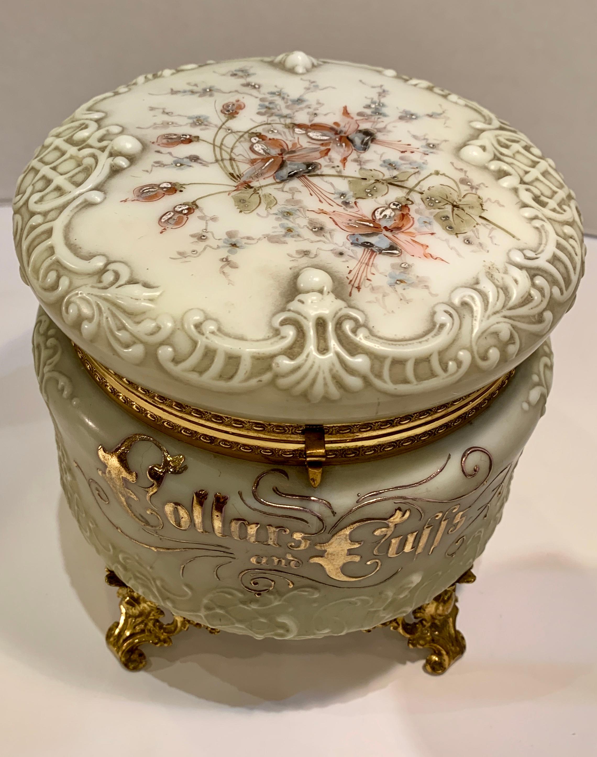 Ornate Victorian, molded high relief opalware glass round box with hinged lid features “Collars and Cuffs” hand painted in raised 24-karat gold on the front and a beaded, raised enamel pastel floral motif on the lid. Box has egg and dart pattern