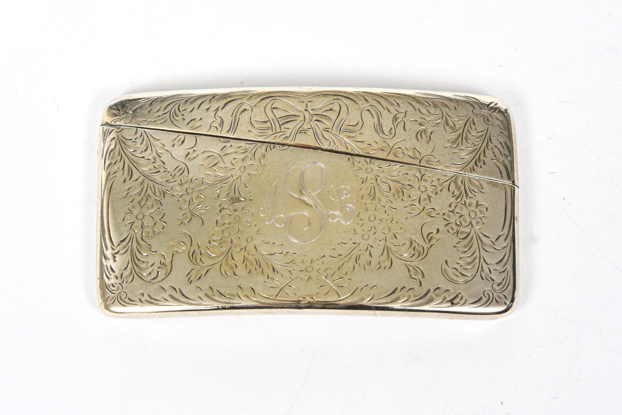 Finely made Victorian sterling silver calling card case featuring an engraved floral design with a bow centrally set on the top of the area with a monogram. The monogram looks like MSL to me. It is curved design. One side is engraved and the other
