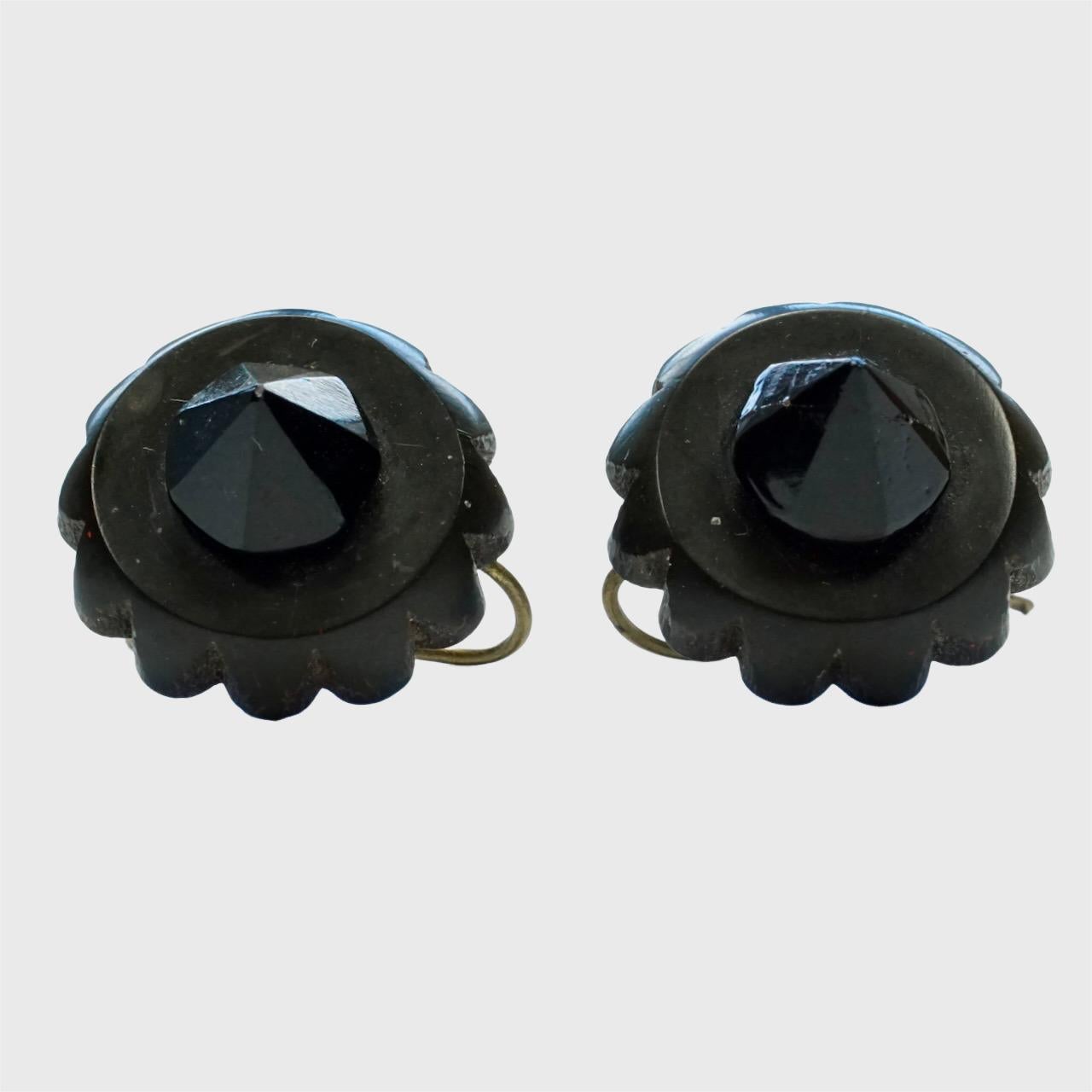 Antique pair of earrings featuring Whitby Jet with contrasting shiny black glass tops. They have gold tone hooks. Measuring diameter 1.6 cm / .6 inch. 

This beautiful pair of Whitby Jet earrings is from the Victorian era.