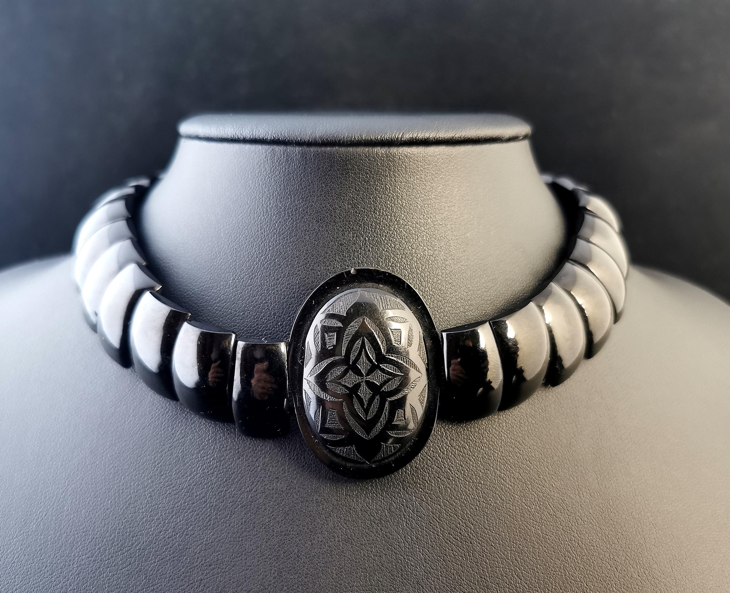 A stunning antique Victorian era Whitby Jet choker necklace.

It is made up from high polished rectangular, domed Whitby Jet beads with a large engraved centre pendant bead with an Arts and Crafts style design.

It fastens with a black japanned