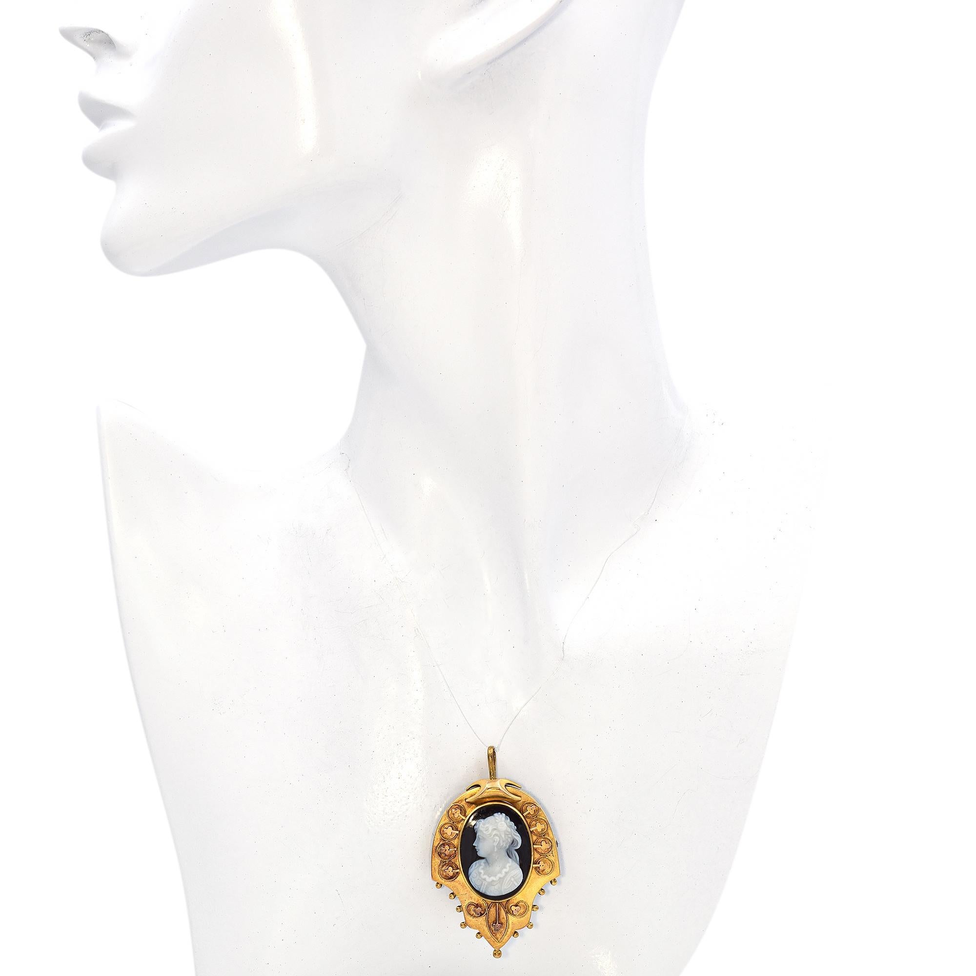 This captivating piece is crafted in yellow gold, showcasing an elegant and ornate framework.
At the center is a finely detailed cameo, depicting a lady profile in white against a dark hardstone background.
The surrounding gold frame features