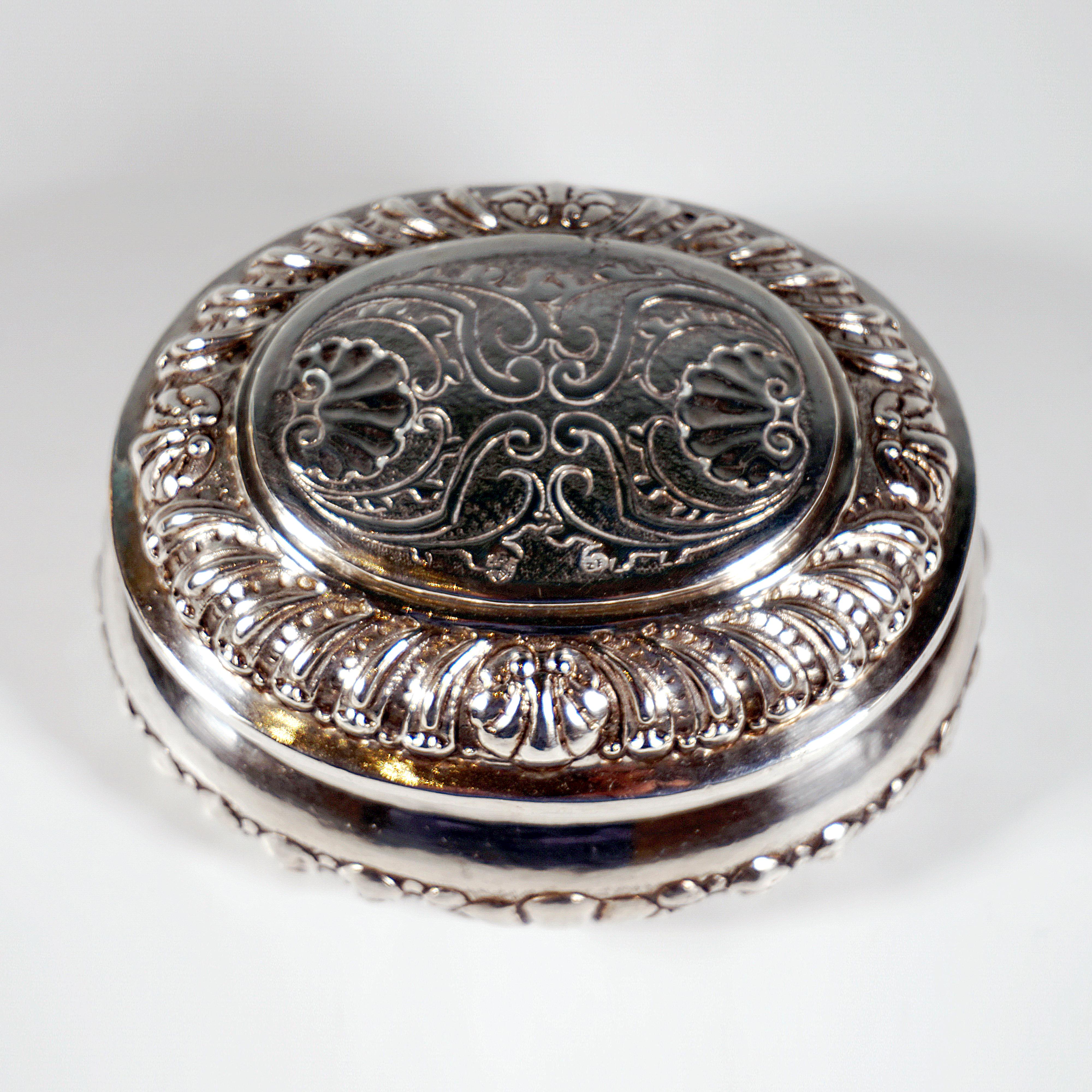 Caja barroca de plata con tapa de tapón suelta de forma oval bulbosa, soporte enrasado sin pies, en la zona inferior del recipiente y en la tapa decoración en jefe cincelada con ornamentación, entre bivalvas, hendidura lisa en las aberturas, parte