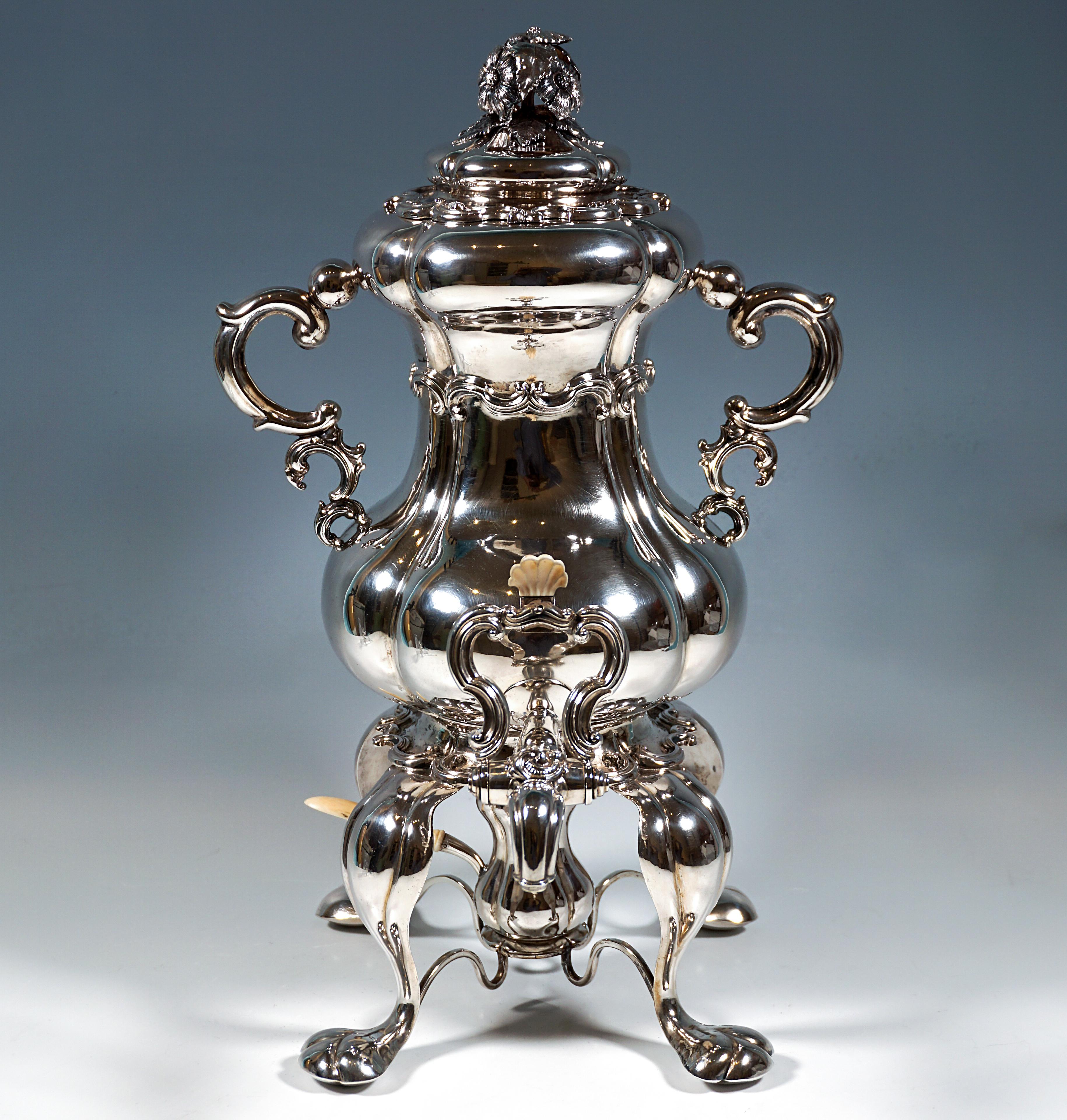 Festive silver samovar consisting of a hot water vessel with a lockable spout, rechaud frame and burner.
Pear-shaped vessel with four vertical folds, rocaille relief band around the constriction, tall rocaille handles protruding on the sides, crane