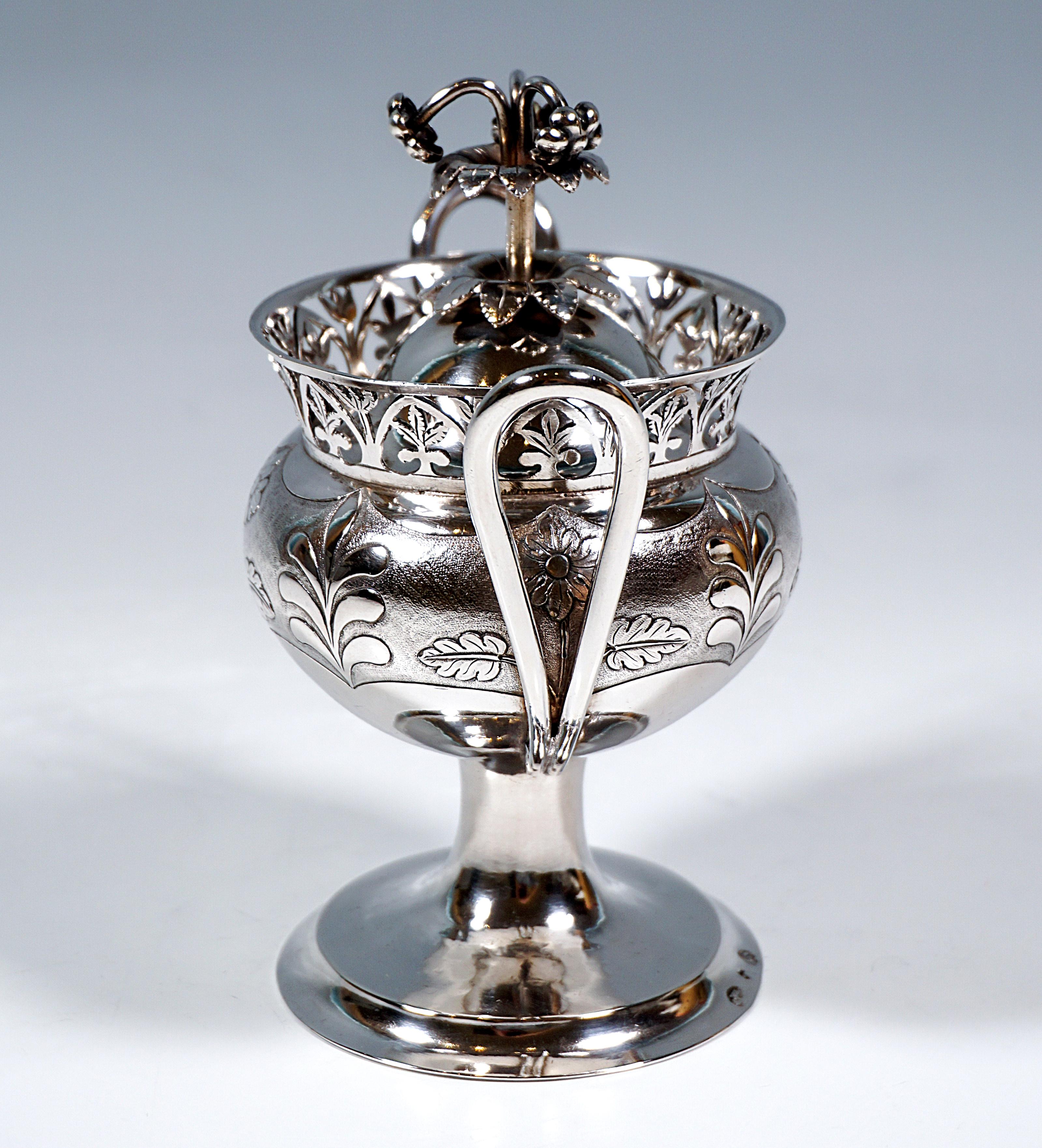 Azucarero imperio de plata, cuerpo bulboso prensado sobre una base redonda alta y desplazada con borde acanalado; la mitad superior del recipiente está cincelada con flores y decoración de hojas emplumadas, arcos elevados a ambos lados a modo de