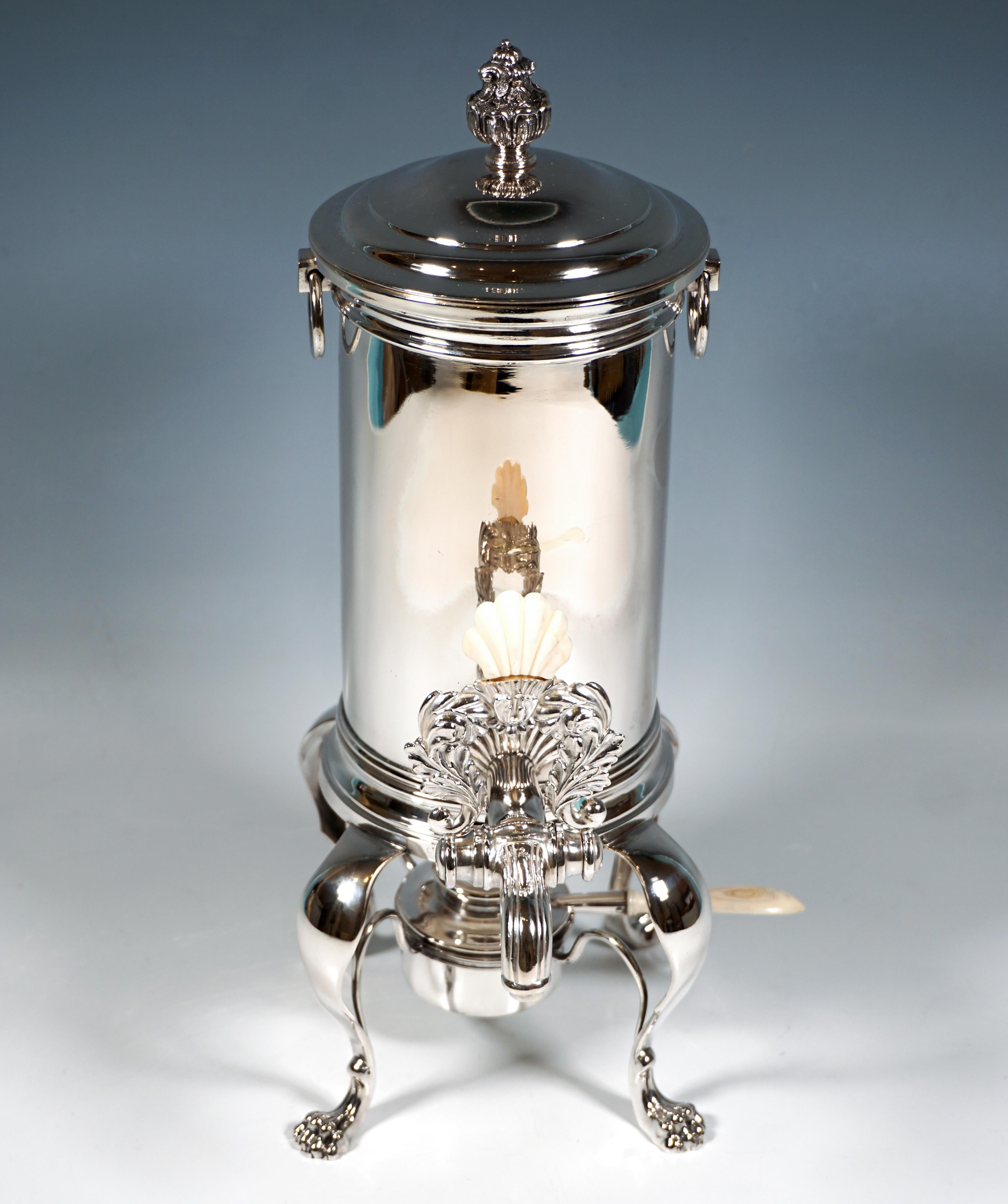 Compuesto por un recipiente de agua caliente con boquilla bloqueable, una trébede y un quemador.
Recipiente cilíndrico con dos asas en forma de gota, tapa desmontable con pomo en forma de jarrón con ramo de flores, palanca de pico con decoración de
