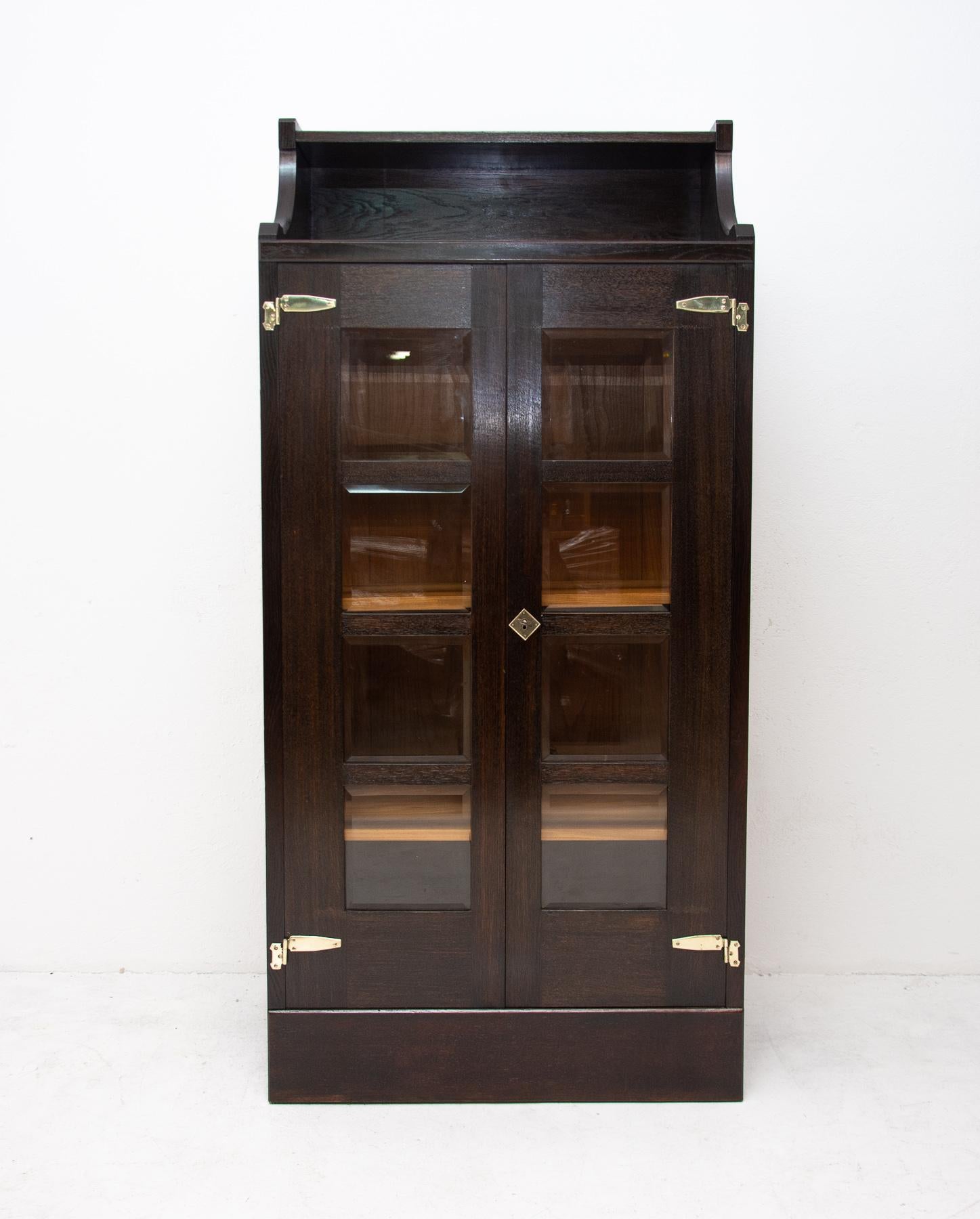 This secession cabinet was produced in Austria-Hungary, circa 1910. It is made of dark stained oakwood. It features storage at the top. It has a beautiful brass fittings with decorative Art Nouveau elements that have been completely cleaned. The