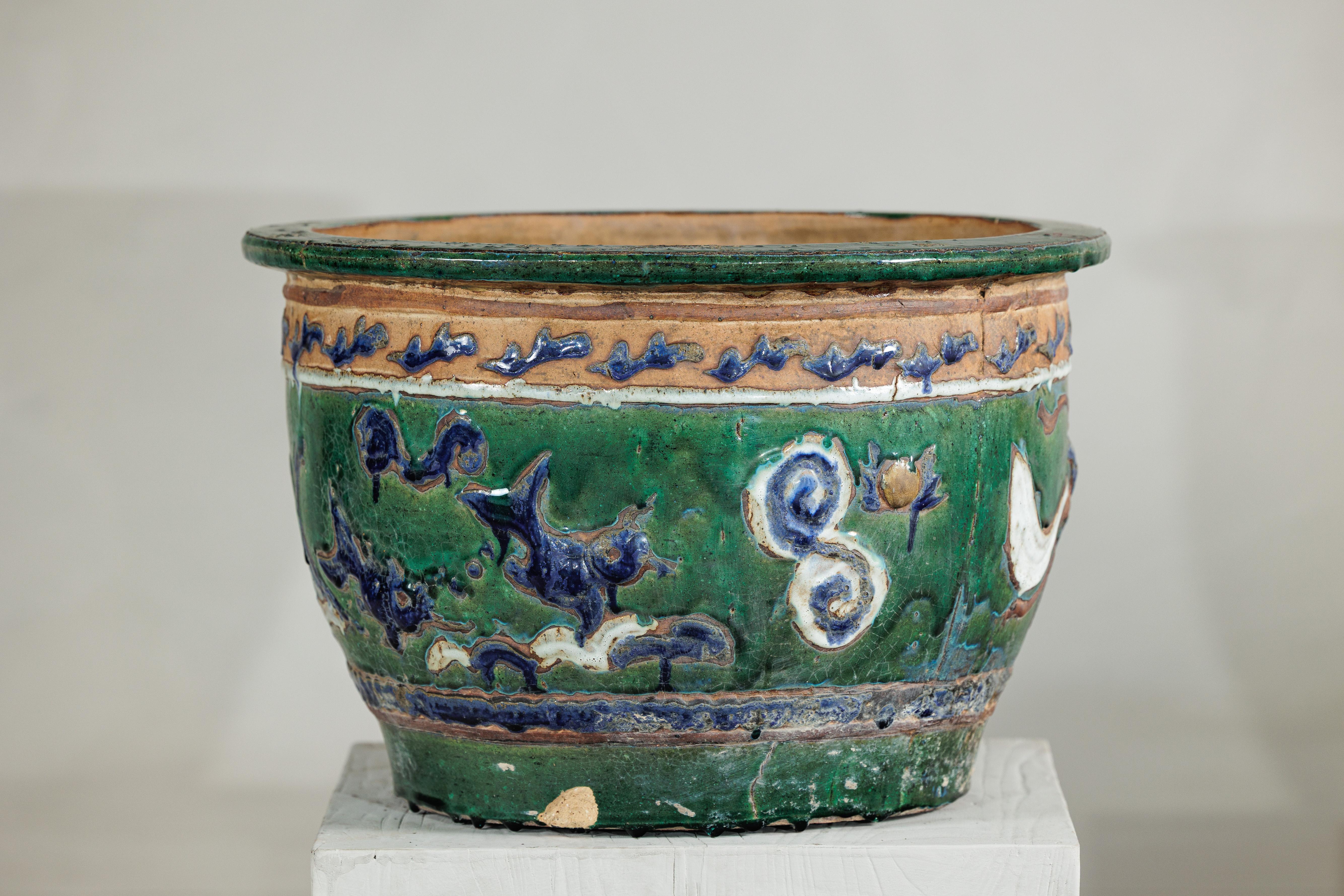 Cette ancienne jardinière en céramique vietnamienne, originaire de l'Annam, est ornée d'une riche glaçure verte accentuée par des détails bleu cobalt et crème. Le corps est décoré de dragons en volutes et de formes nuageuses en relief, ce qui lui