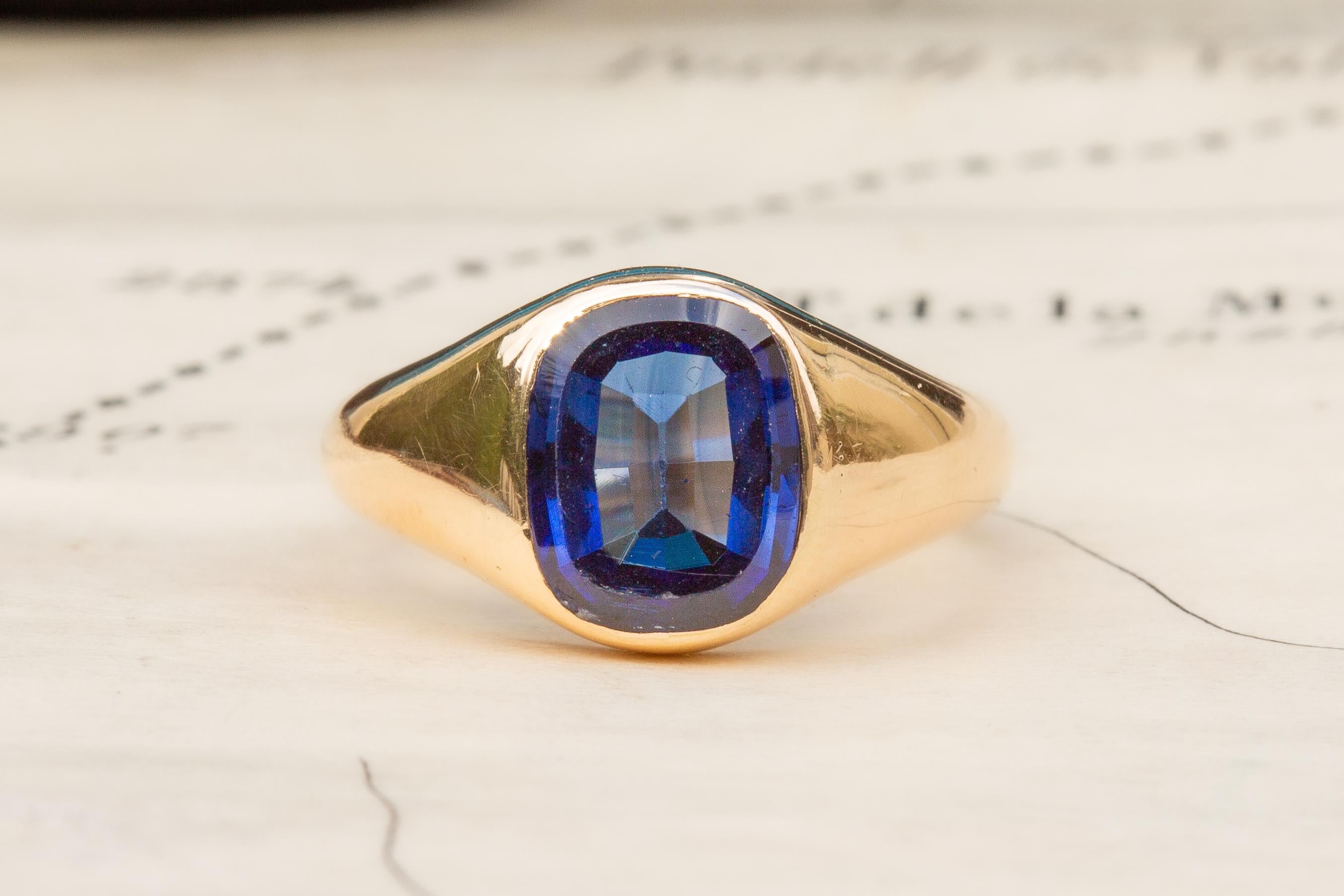 A gorgeous gold sapphire signet ring, circa 1940’s. The centre of the beautifully silky gold ring is bezel set with an oval table-cut synthetic sapphire which displays a royal blue colour and weighs approximately 2.3ct. The setting is open to the