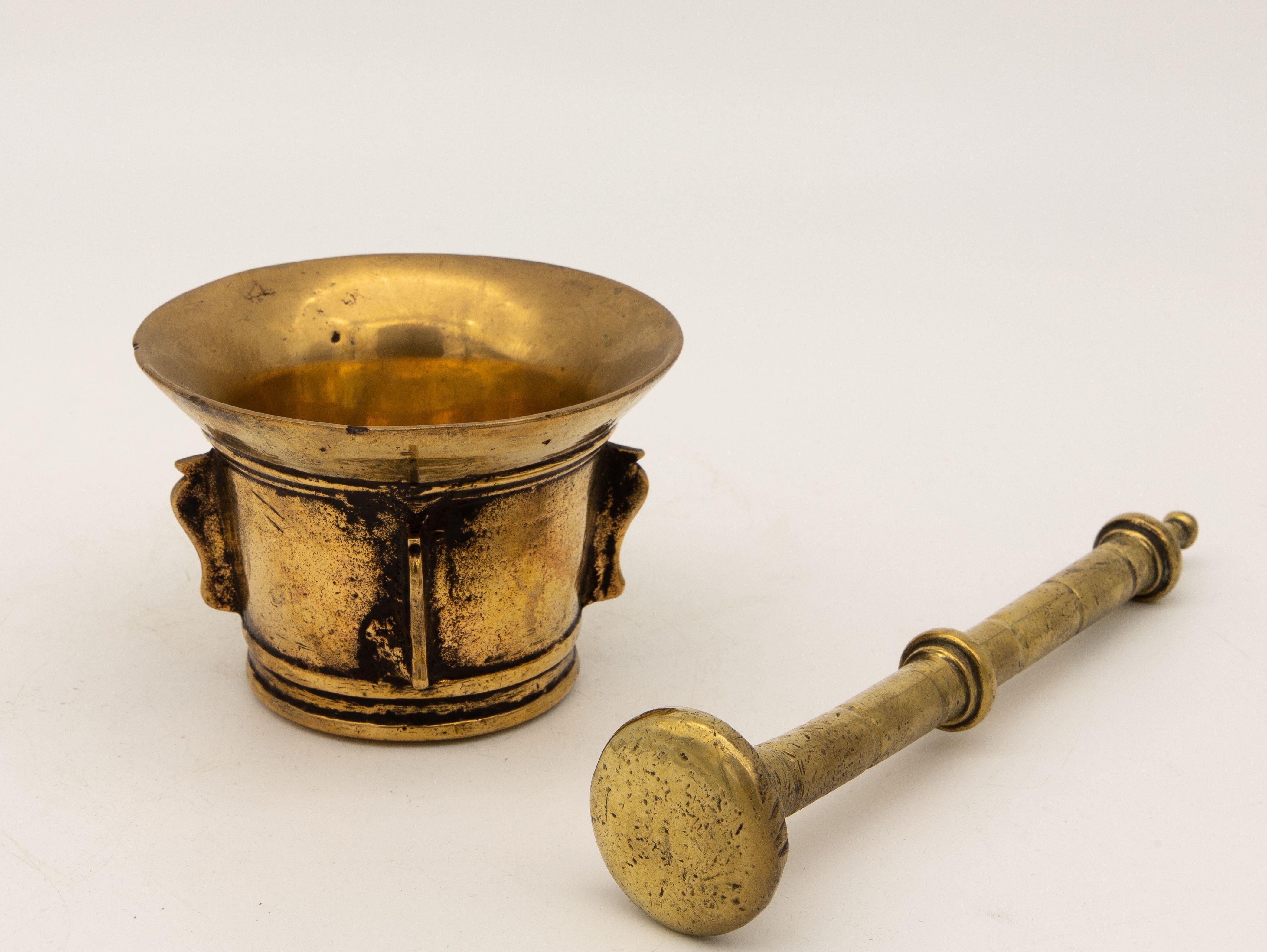 This early 20th-century mortar and pestle is made of brass with an honest patina. Both the mortar and pestle are traditional in style. The mortar has a classic bell-shaped body and the pestle has one rounded end. Brass mortar and pestles were used