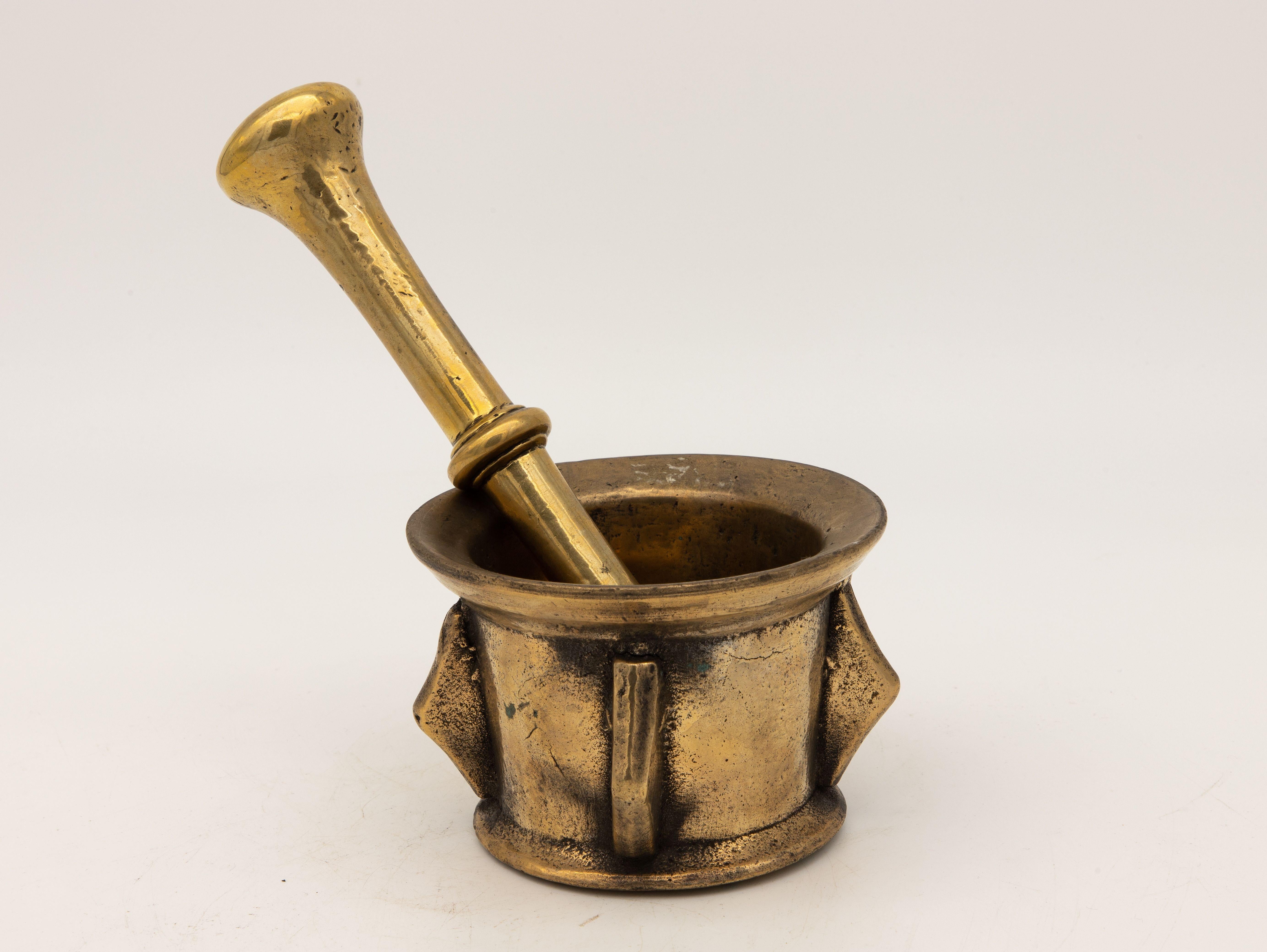This early 20th-century mortar and pestle made of brass with an honest patina. Both the mortar and pestle are traditional in style. The mortar has a classic bell-shaped body typical of the style and the pestle has round ends on each side. Brass