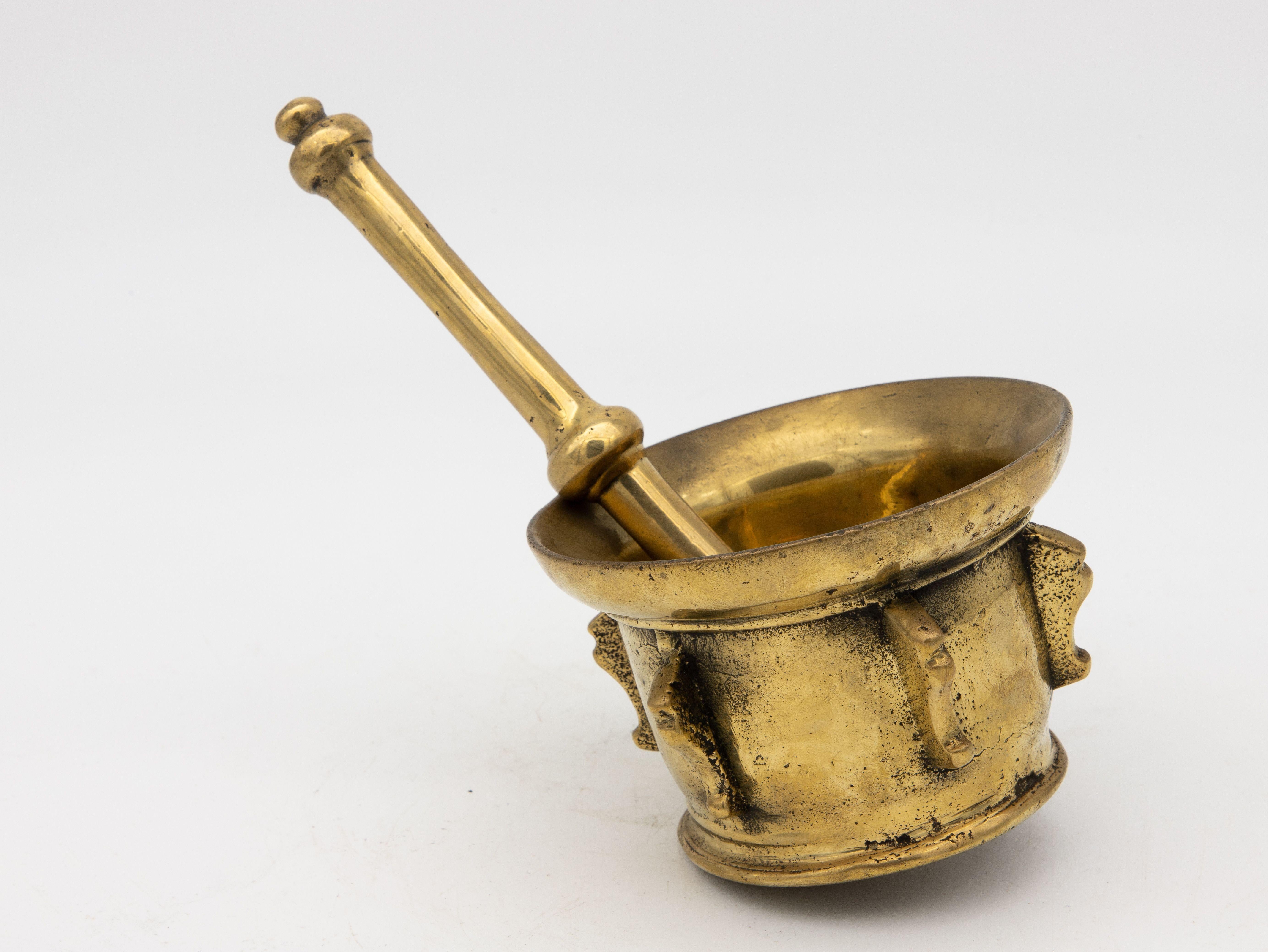 This early 20th-century mortar and pestle is made of brass with an honest patina. Both the mortar and pestle are traditional in style. The mortar has a bell-shaped body with a rounded base this style is known for, and the pestle has one round end.