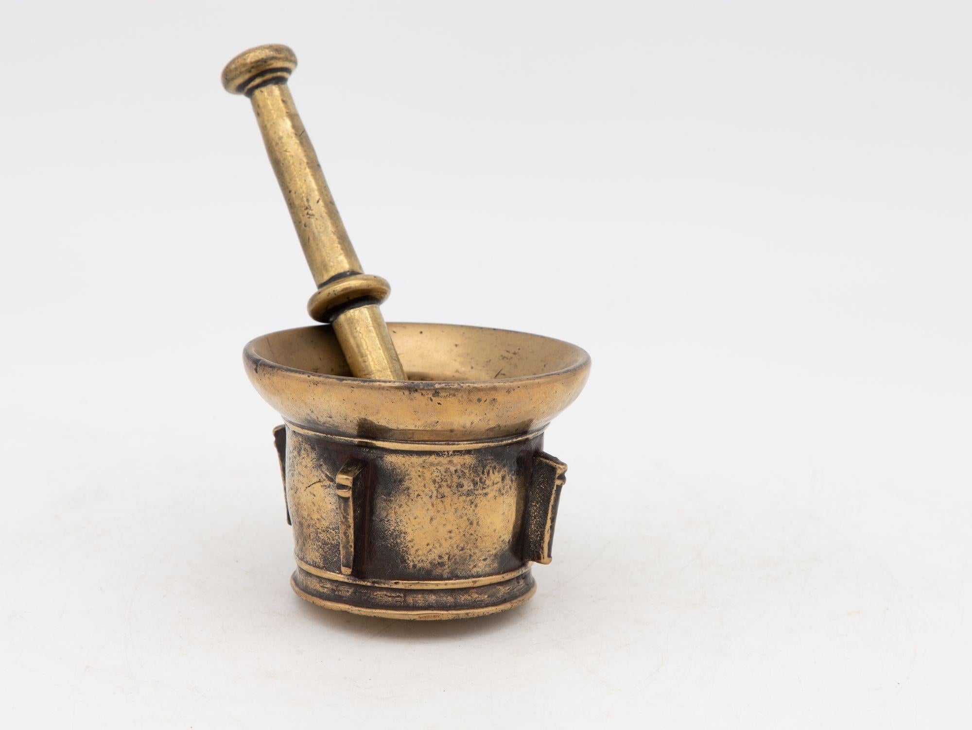 This early 20th-century mortar and pestle is made of brass with an honest patina. Both the mortar and pestle are traditional in style. The mortar has a classic bell-shaped body and the pestle has two rounded ends. Brass mortar and pestles were used