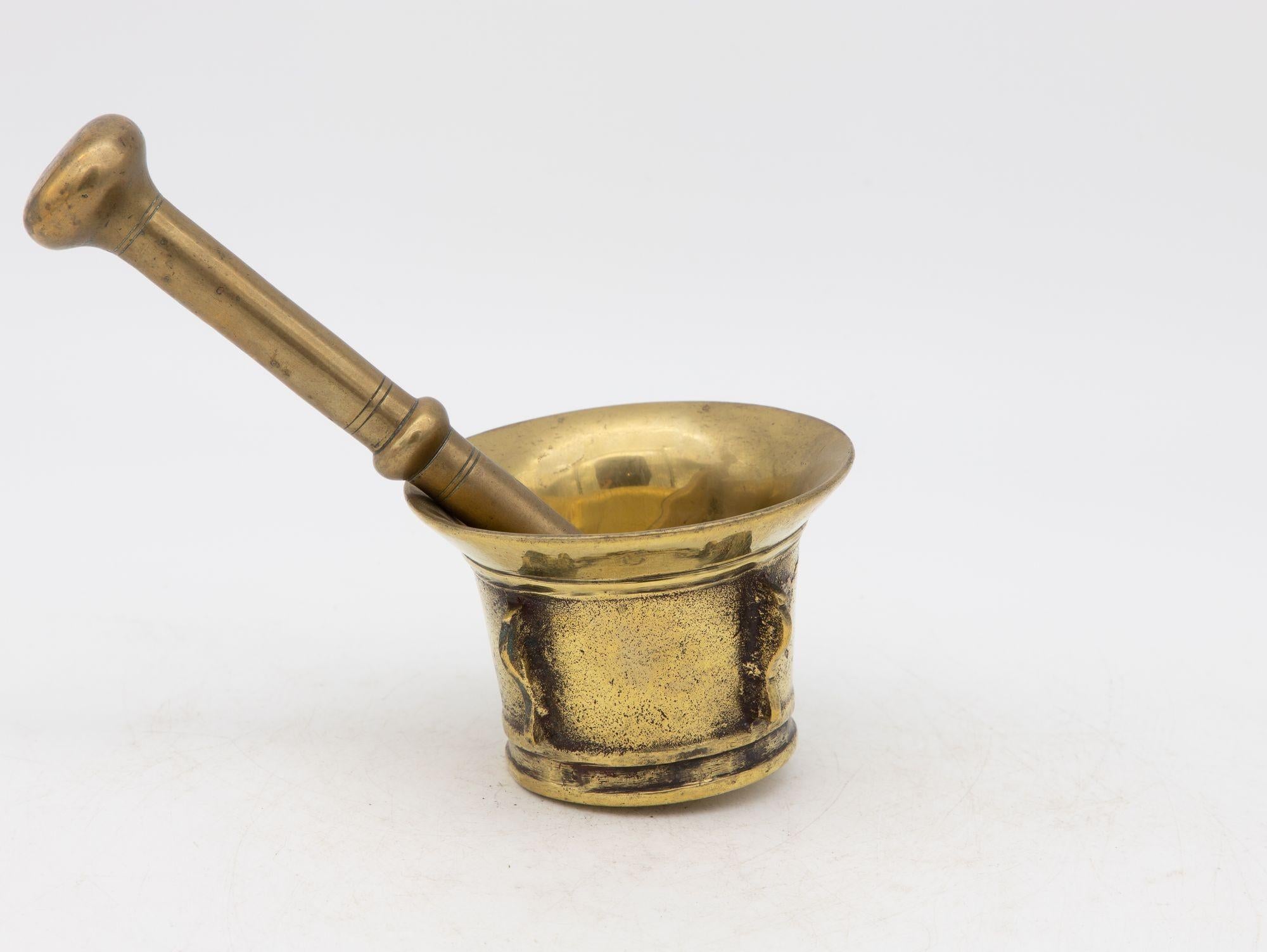 This early 20th-century mortar and pestle is made of brass with an honest patina. Both the mortar and pestle are traditional in style. The mortar has a classic bell-shaped body and the pestle has two flat ends. Brass mortar and pestles were used for