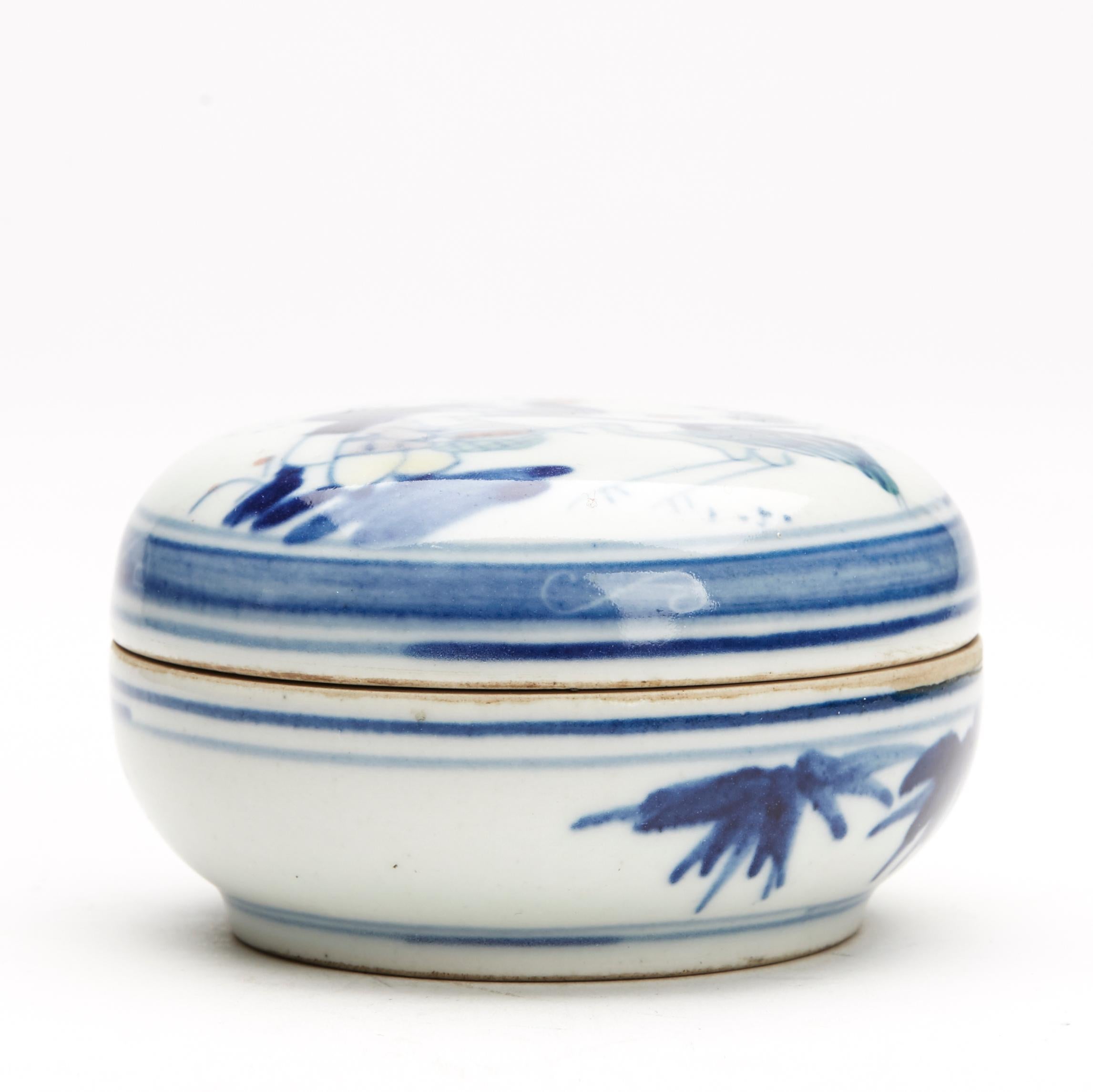 A Chinese porcelain lidded box of rounded form decorated with a figural scene of a man and child, the child feeding a bird decorated in Wucai glazes. The inner box has a further figural design and the box stands on an unglazed foot with unglazed