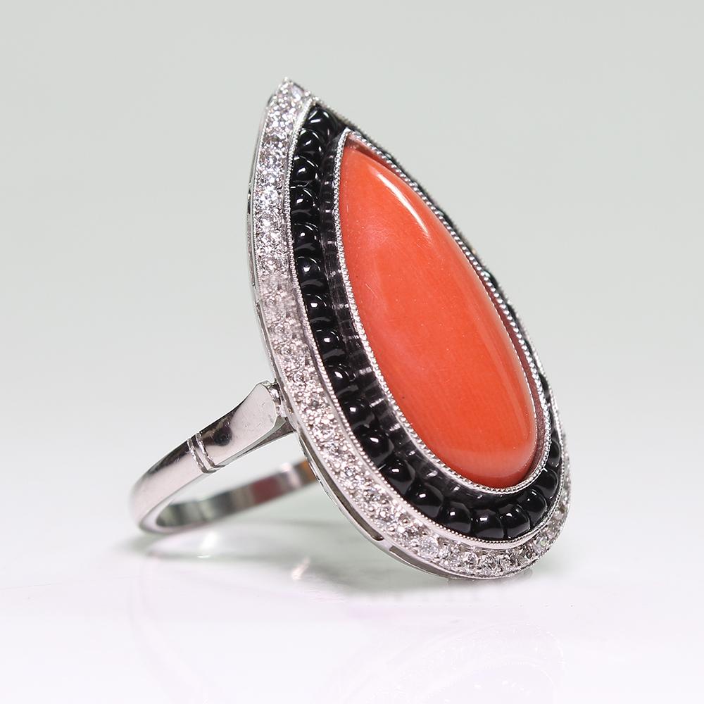 Showcasing one (1) Pear Shaped Red Coral Cabochon, measuring 20.27 x 10.10 x 4.48 mm, weighing approximately 6.68 carats.  
Thirty (30) Round Cabochon Black Onyx gemstones accent the center coral in a halo design.
A halo of fifty (50) Old European