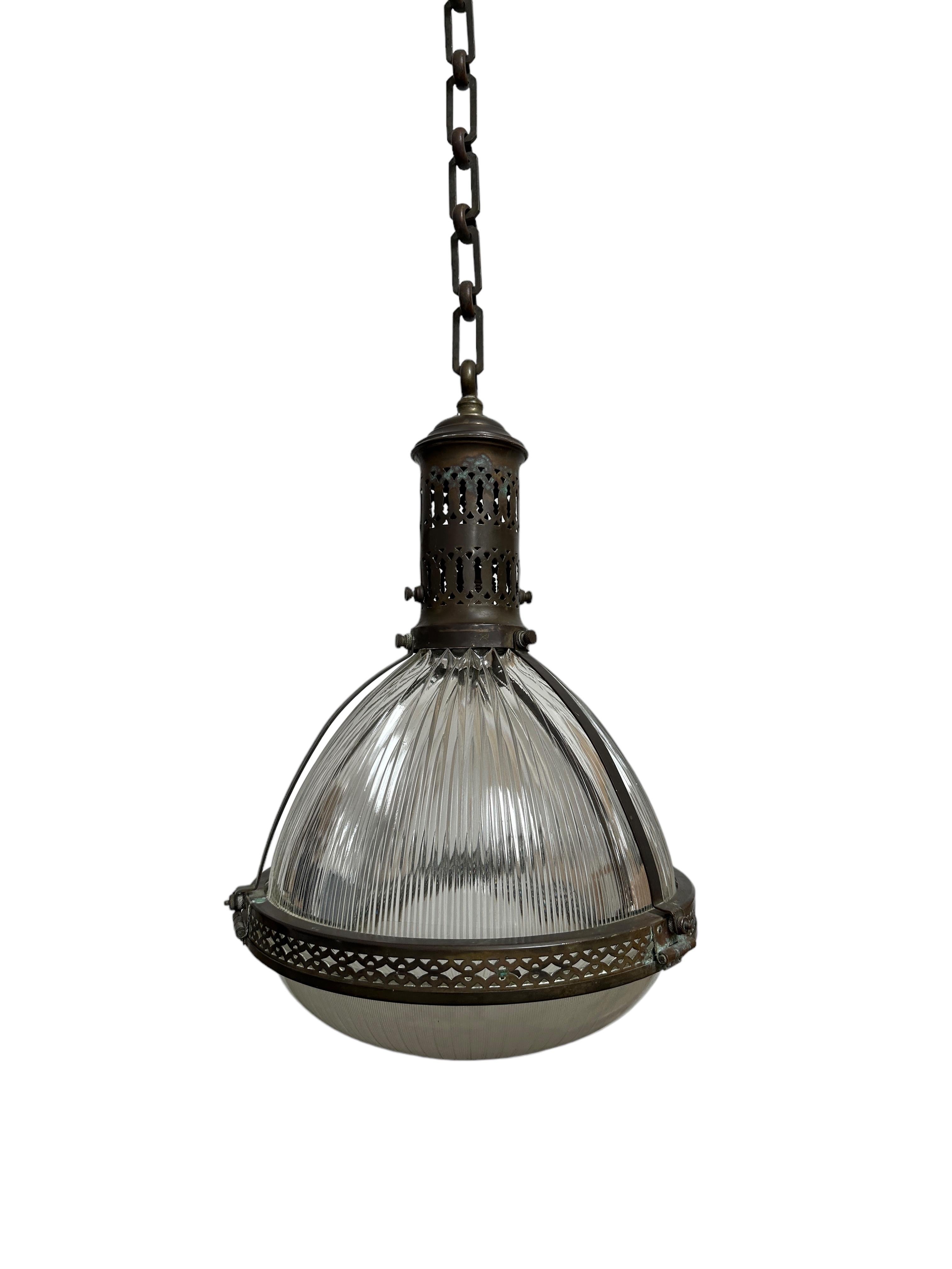 - An outstanding and extremely rare large caged Holophane pendant with original chain and ceiling rose, France circa 1920.
- Heavy brass cage housing two sections of prismatic glass, both stamped Holophane.  The cage is hinged around the rim in