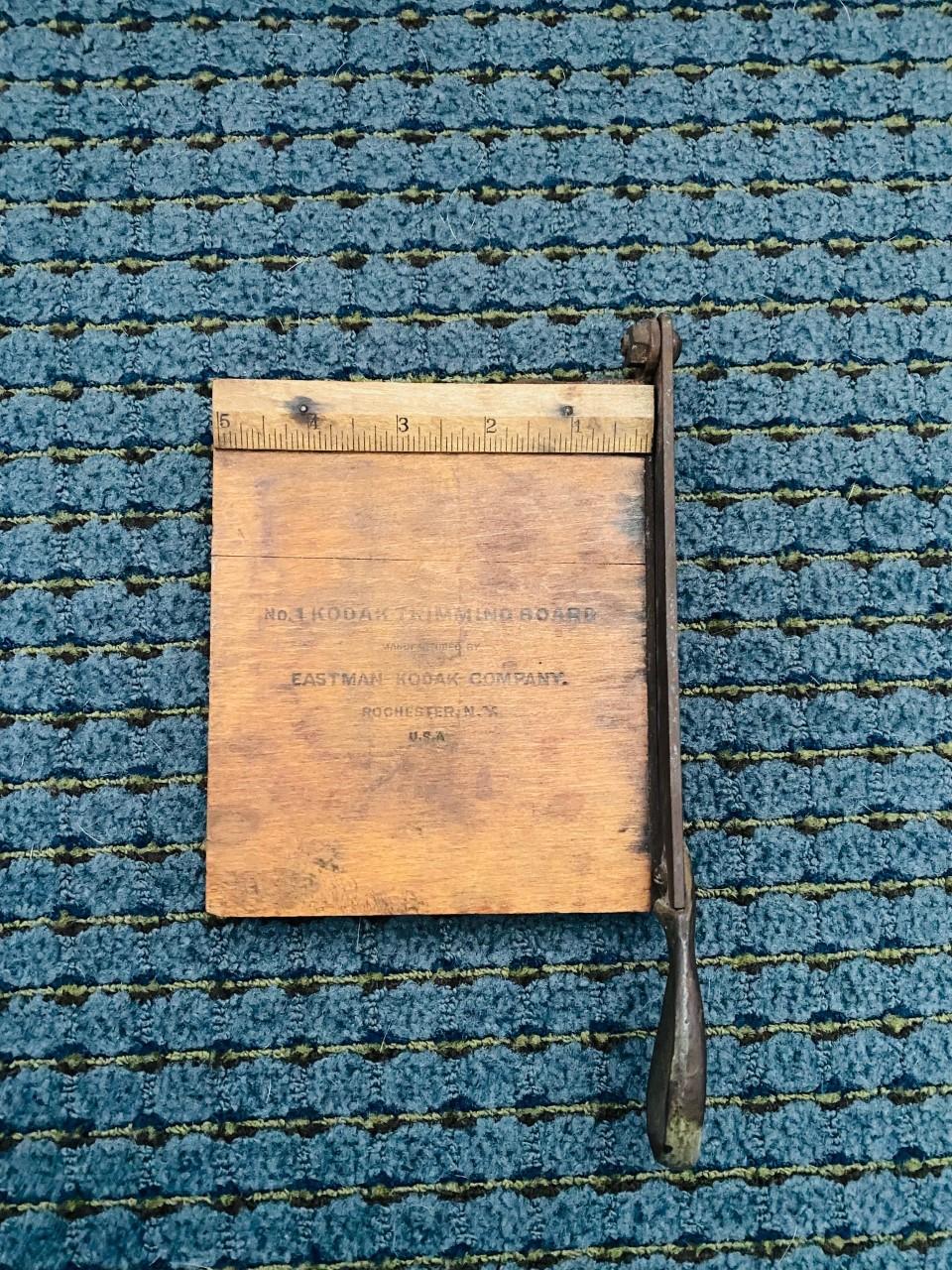 Antique vintage kodak wooden trimming board by Eastman. The wooden cutting surface measures 6 inches tall by 5 inches wide by 3/4 inches tall. Some of the original writing can be seen on the surface of the board and the ruler on the top is visible.