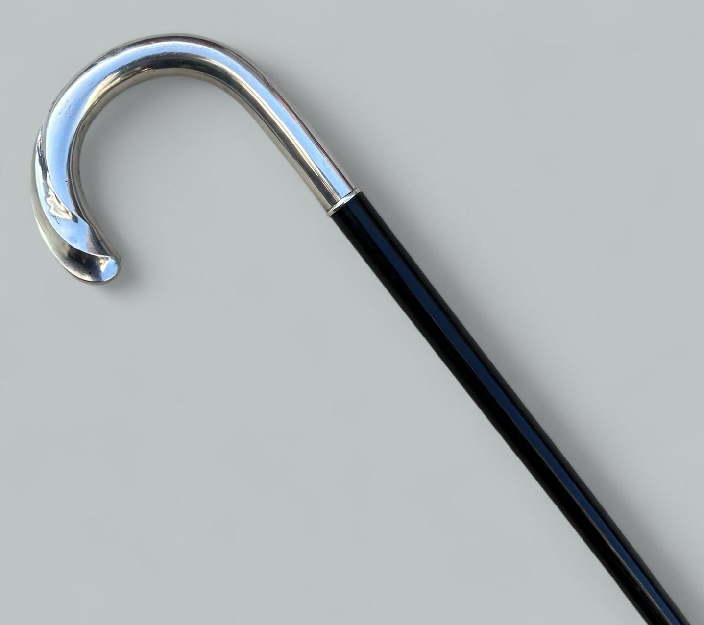 Elegante bastón de dama o caballero de ébano macizo pulido y plata de ley, con empuñadura tradicional en forma de cayado de origen alemán, completo con su virola original bimetálica de latón pulido y acero, muy ligeramente desgastada por el uso.