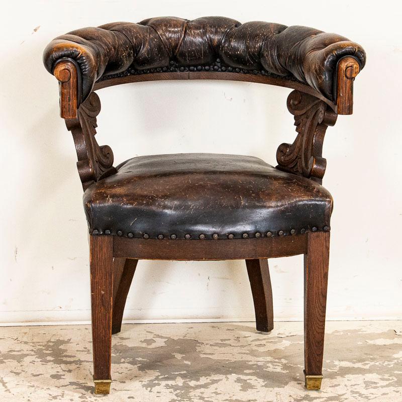 The leather is all authentic vintage in this handsome curved and carved office chair. Notice the rounded and tufted back that encircles the sitter, and the carved sides that support it. The carving is reflective of the late 1800s, while the legs