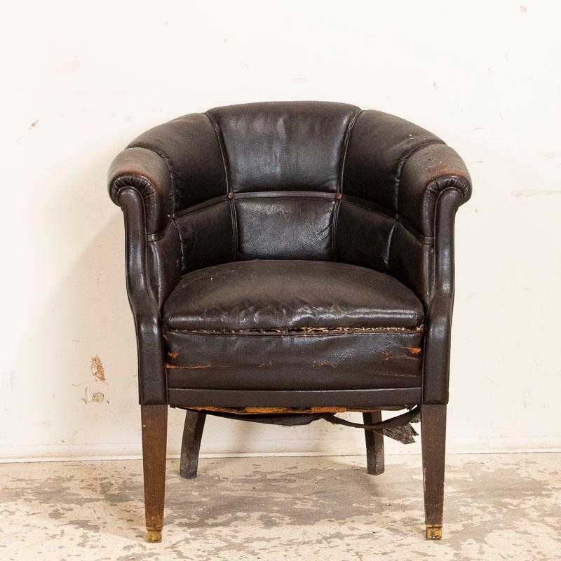 The rolled arms and back of this vintage brown leather arm chair are accented by leather strips which adds to their visual appeal. There is extensive age related wear to the leather with cracking and separation at seam of seat, etc. Scratches and