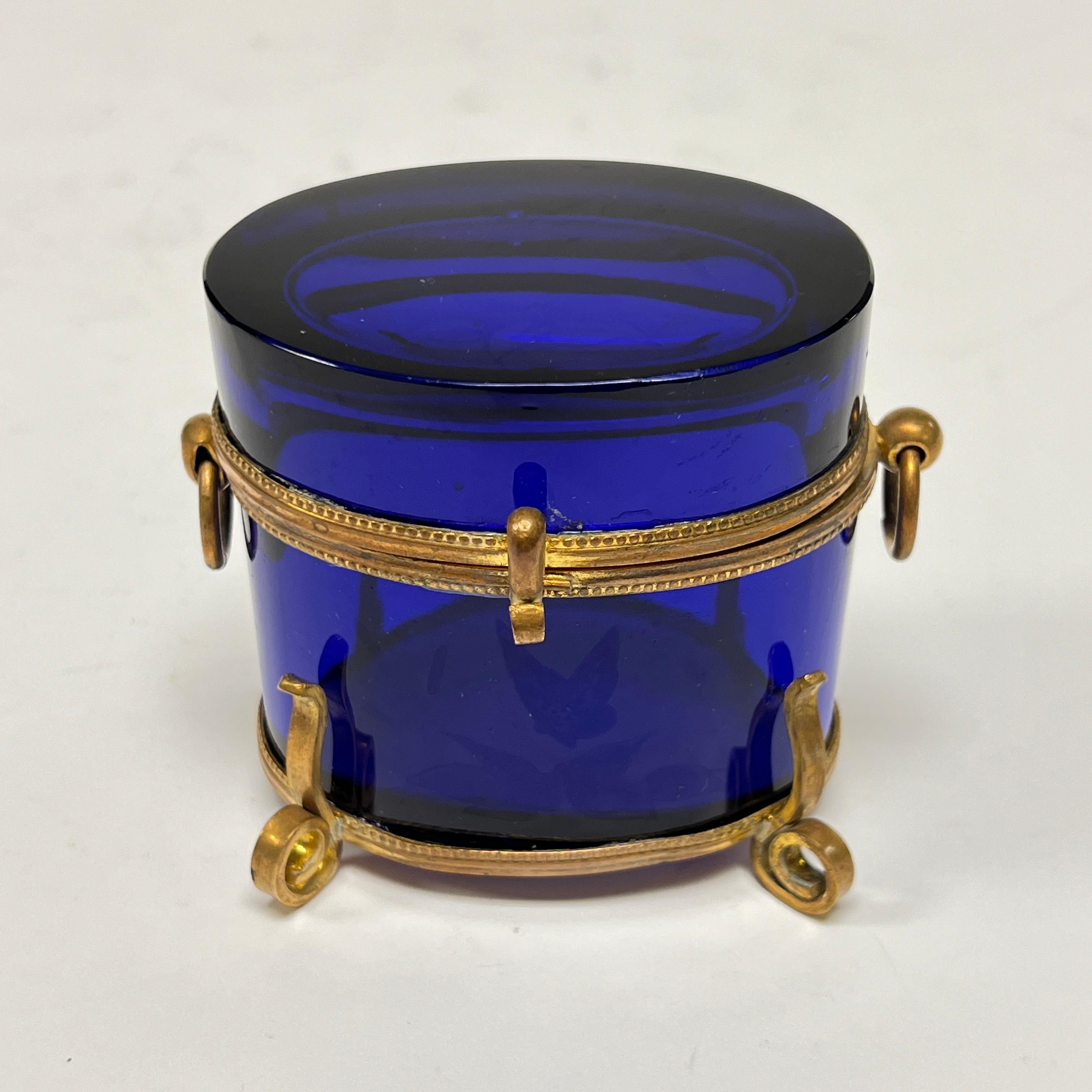 Beautiful antique (late 19th century) oval-shaped jewelry or trinket box crafted from violet/blue glass with gilt bronze frame.  3 1/2 in wide, 3 in tall and 2 1/2 in deep.
