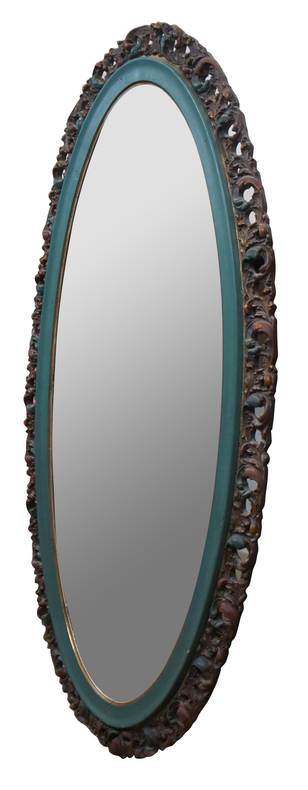 Antique early 20th century beveled oval wall mirror by the Von Gerichten Art Glass Co of Columbus, Ohio featuring French or Italian Rococo styling with reticulated or pierced accents and painted wood frame carved with swirling leaves in turquoise,