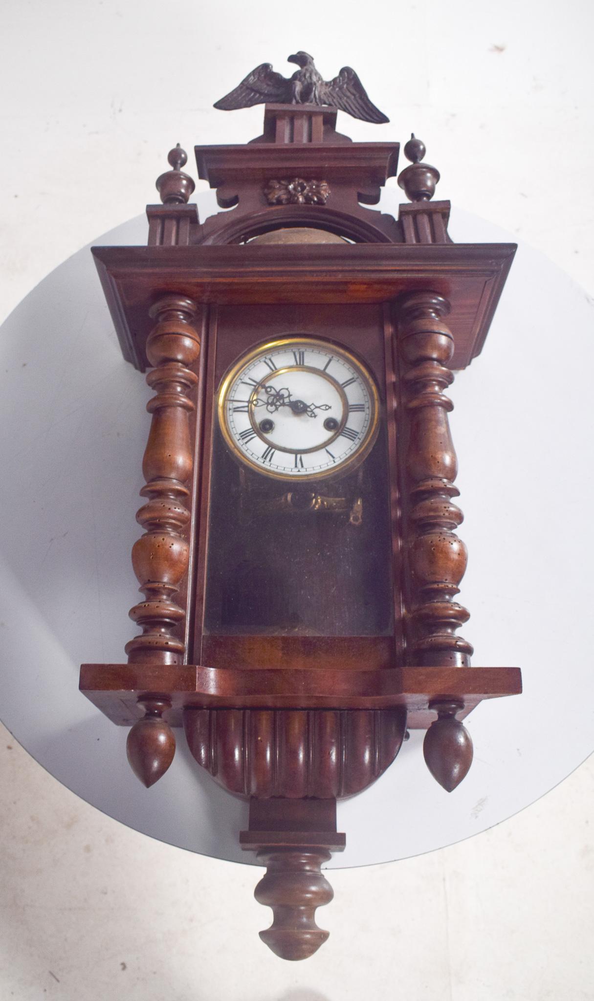 Wall clock with carved Eagle. With carvings and turnings, topped by a floret and an eagle. With an imposing design, with turned lateral columns and carved details at the top, a finial and a carved eagle.
The dial is circular, with a gold frame,