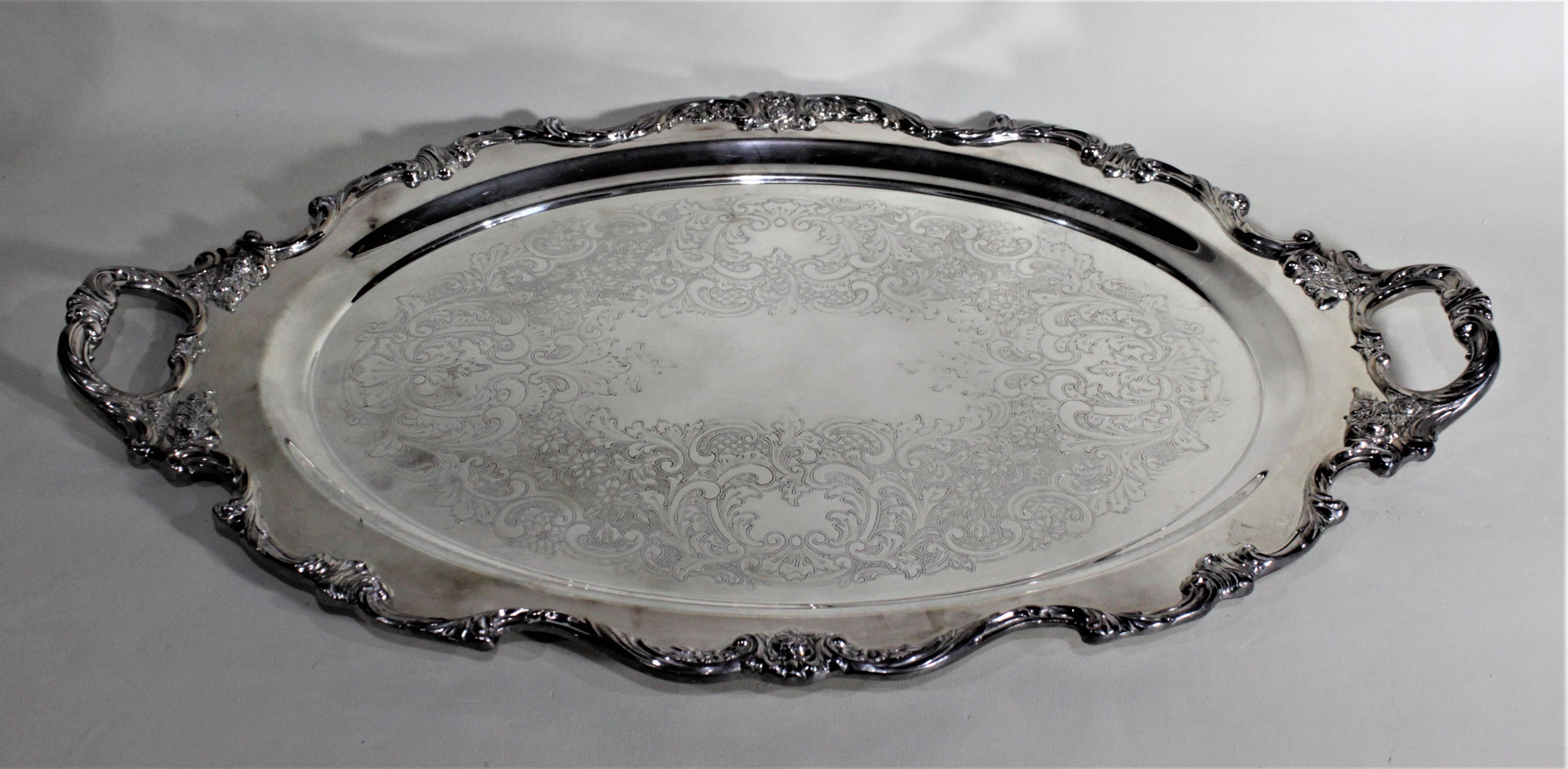 This silver plated serving tray was made by Wallace of the United States in circa 1950 in the Victorian style. This oval tray is done with intricate floral decoration on the sides and handles accented by scrolling leaf and vines. The bottom of the